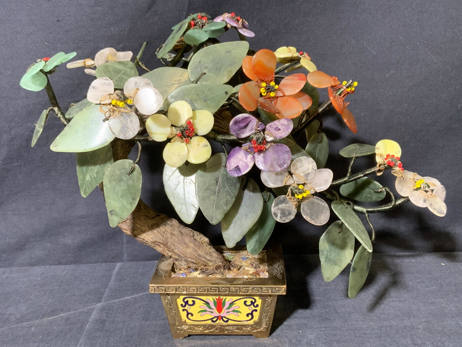 Natural Stone Bonsia Tree Sculpture Cloisonne Base: Cloisonne Planter with Multicolor Stone Flowers, underside reads â€˜made in Hong kongâ€™, subject a multi colored Cloisonne planter with gold toned trim and faux flowers appear to be made of 