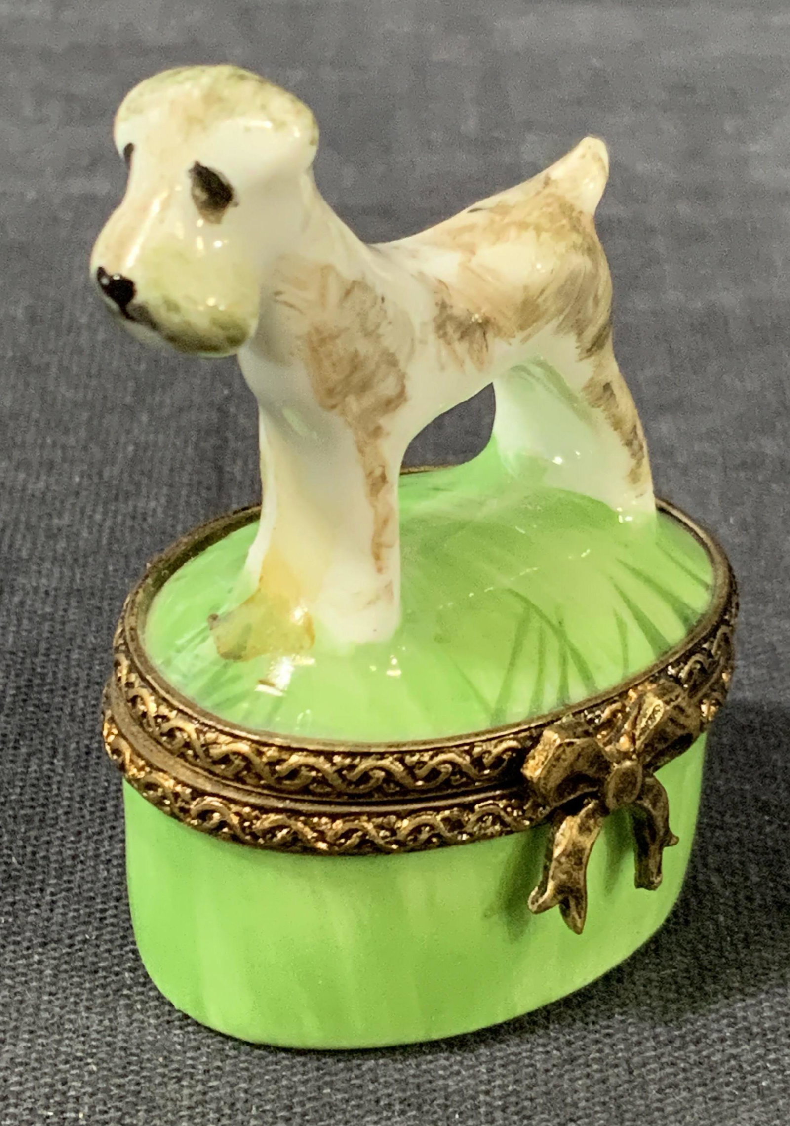 LIMOGES Porcelain Terrier Trinket Box: A small porcelain box painted green with a brass toned metal rim on lid and body with a porcelain figurine of terrier, marked on underside â€˜ Limoges Franceâ€™ with other illegible signature