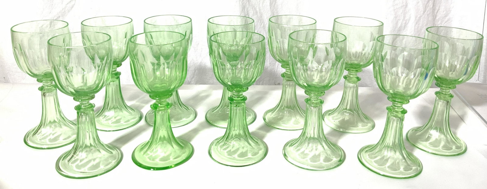 12 PCs Uranium Glass Wine Glasses: A set of 12 small goblet wine glasses made of uranium glass creating the green hue of the glasses. Some glasses vary is height and thickness but all have the same design. The goblets have a scalloped 