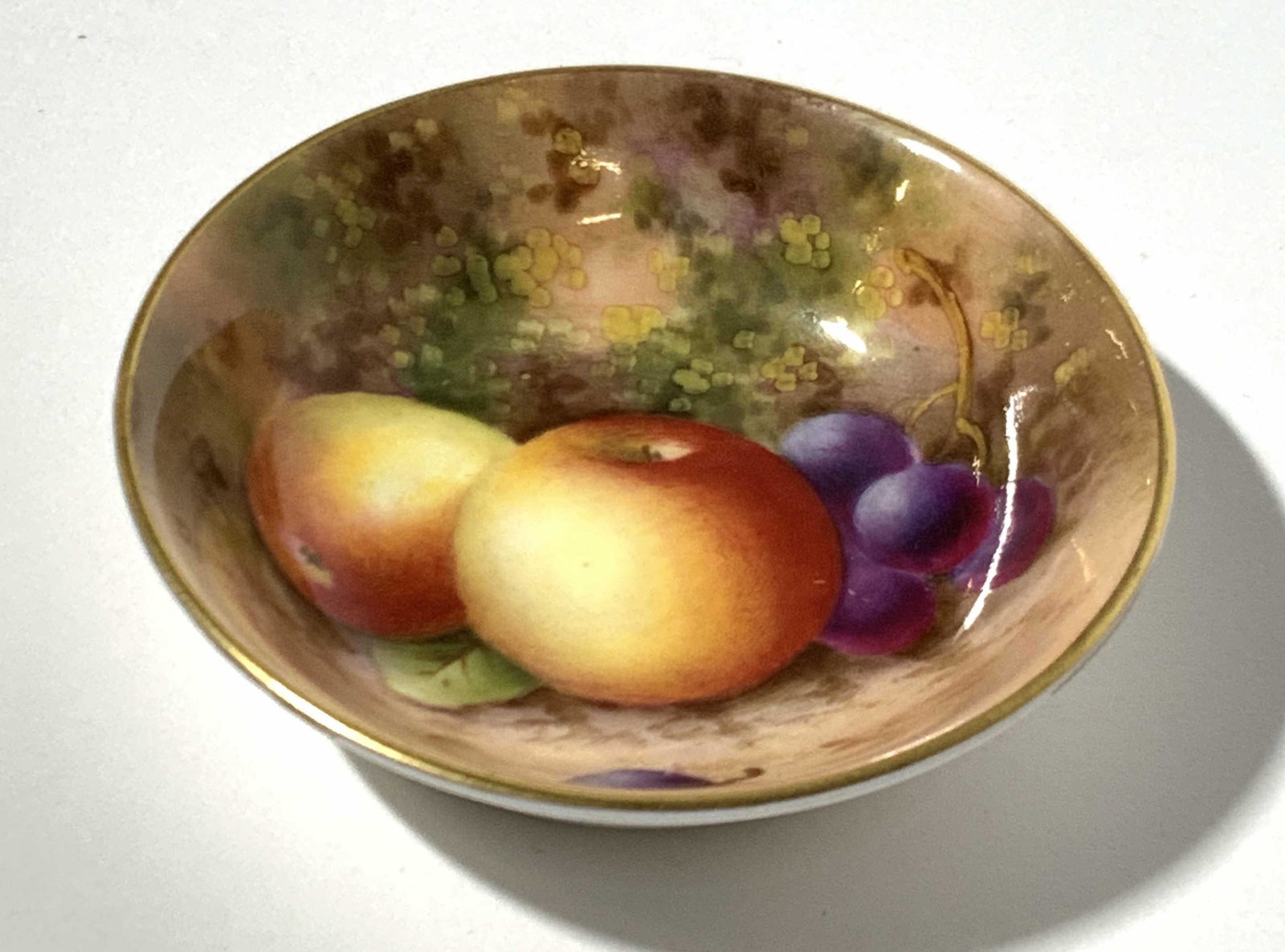 Vintage Royal Worcester Porcelain Trinket Bowl: A vintage small trinket bowl, trademarked on underside Bone China Royal Worcester, made in England with gold gilt rim, and realistic depiction of a still life painting of apples and grapes in center o