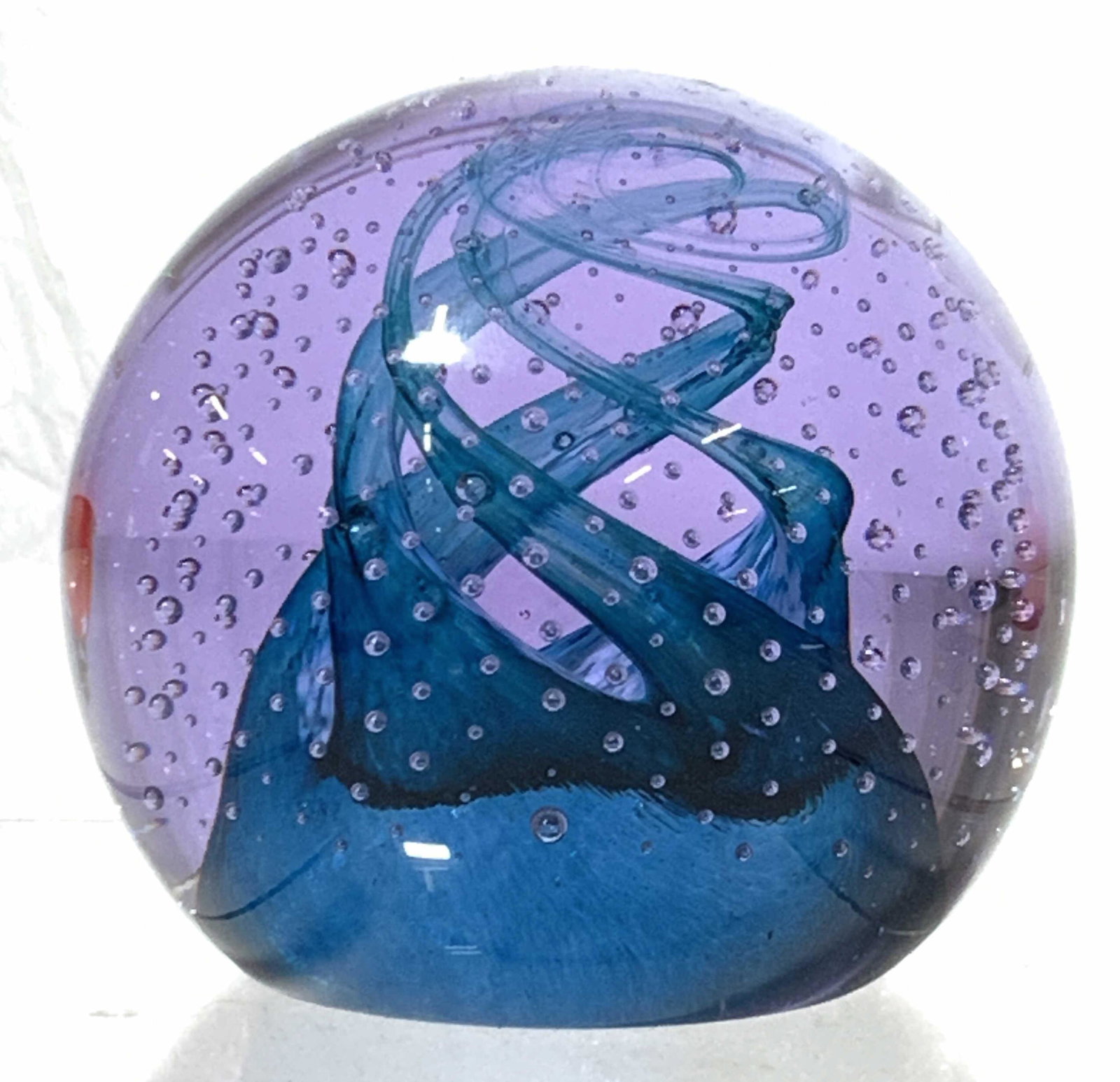 CAITHNESS Art Glass Paper Weight: A glass paper weight signed on underside Caithness Cauldron Aqua Scotland paper weight is made of a purple toned glass with bubbles within, alongside a spiral of blue twisting upward towards the top o