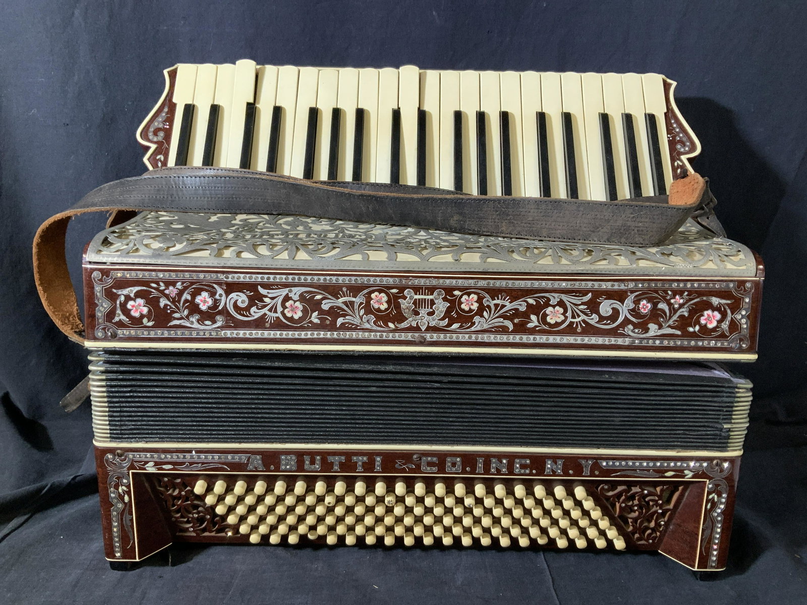 A. BUTTI Co. INC PIANO Accordion Instrument: Natural wood accordion with piano keys and buttons, accentuated with Victorian scrolls, etched with sprig pattern and drizzling in rhinestones. Spelled out in diamante rhinestone is A. Butti Co Inc. N