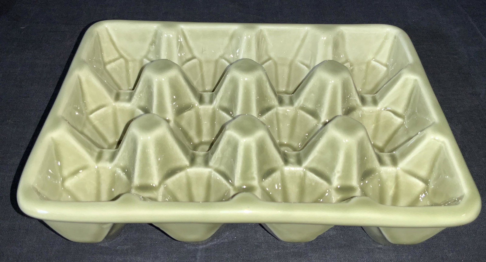 Green Ceramic Egg Carton: An egg Carton bottom made of ceramic with a green tone glaze. Approximately 2.25 in tall and 8.5 x 6.5 in wide. Some wearing to underside. Ceramicware, decorative ceramic decor, ceramic egg carton, eg