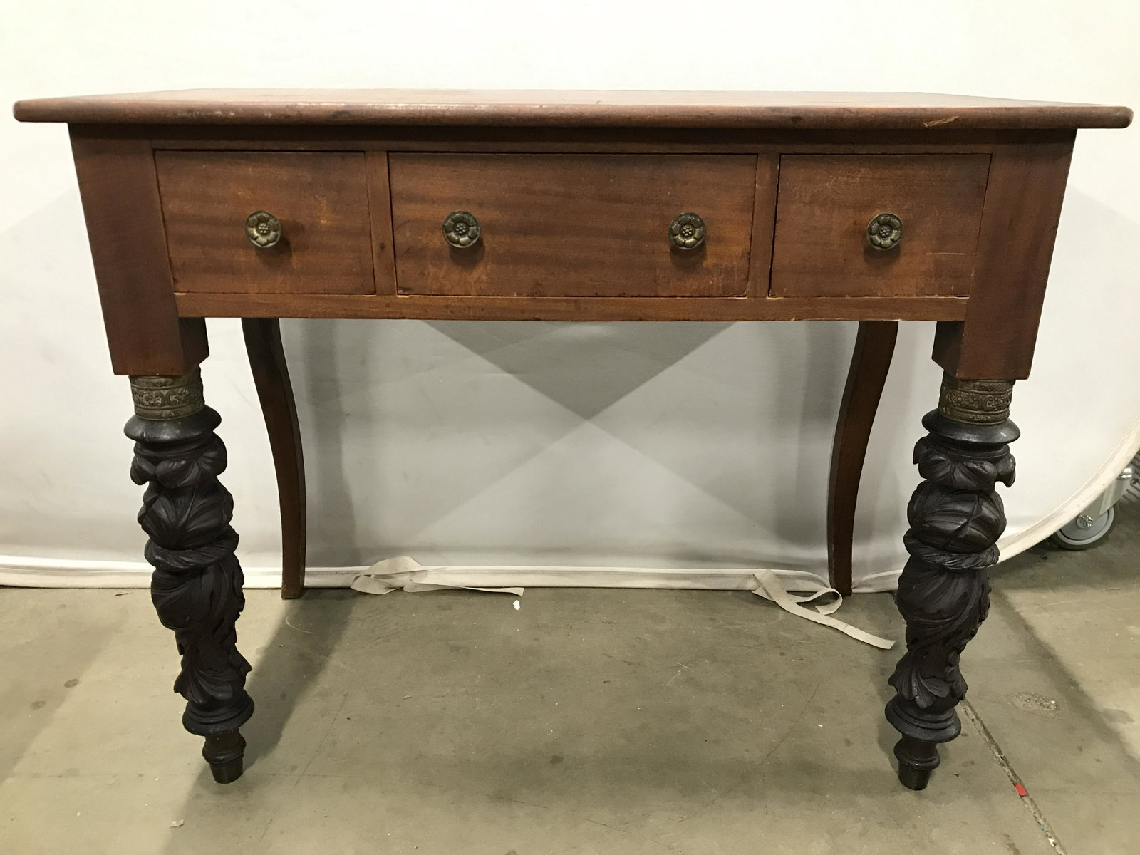 Intricately Carved Vintage Wooden Desk: Desk is vintage possibly antique. Legs of desk have intricately carved detail. Desk has 3 drawers each have hand dovetailing and gold toned brass floral detailed knob style handles. Piece is possibly 