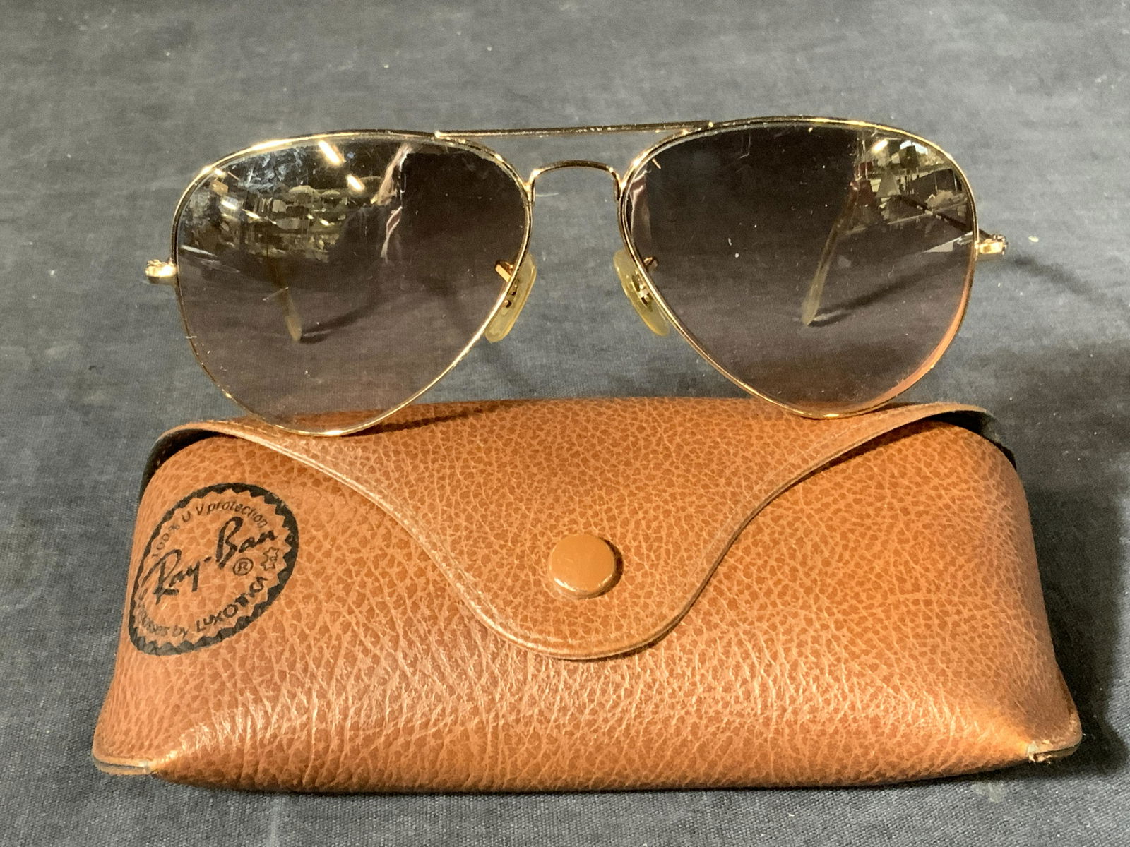 Aviator Sunglasses By Ray-Ban: A pair of aviator sunglasses with gold toned metal frames and arms marked Aviators L on one arm and Rayban Made in Italy, that come in a button case, appears to be leather, marked Ray-Ban on the exter