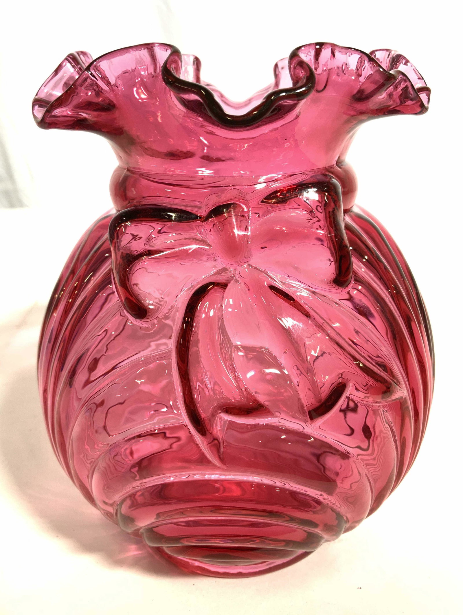 Vintage Cranberry Glass Art Glass Vase: Vase is vintage and cranberry toned. Piece has frilled rim and scalloped edges with bow shaped beveled detail. Vase measures approx 6.5 inches tall 5.5 inches wide. Vase, vintage vase, cranberry glass