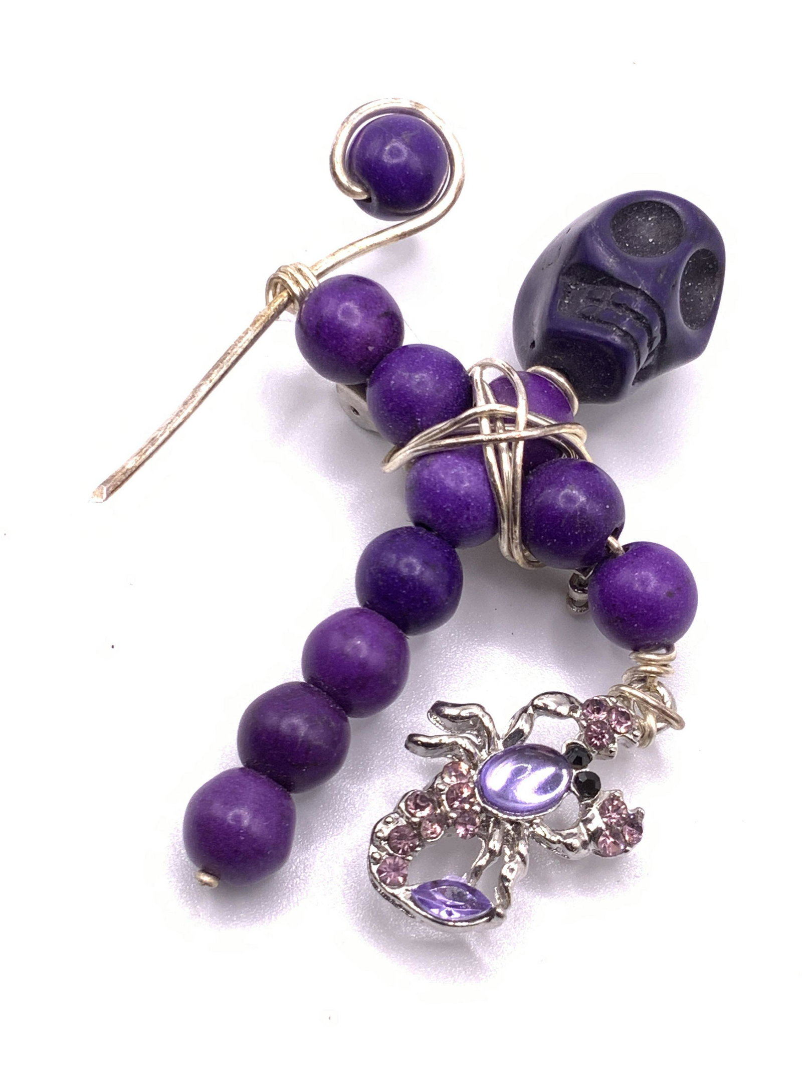 Handmade Skeleton Form Wire Wrapped Brooch: A purple composite bead skeleton form wire wrapped brooch. The skeleton holds a scepter in one hand and a bejeweled scorpion in the other. Reverse possesses metal pin closure. Measures approx 2.5L x 2