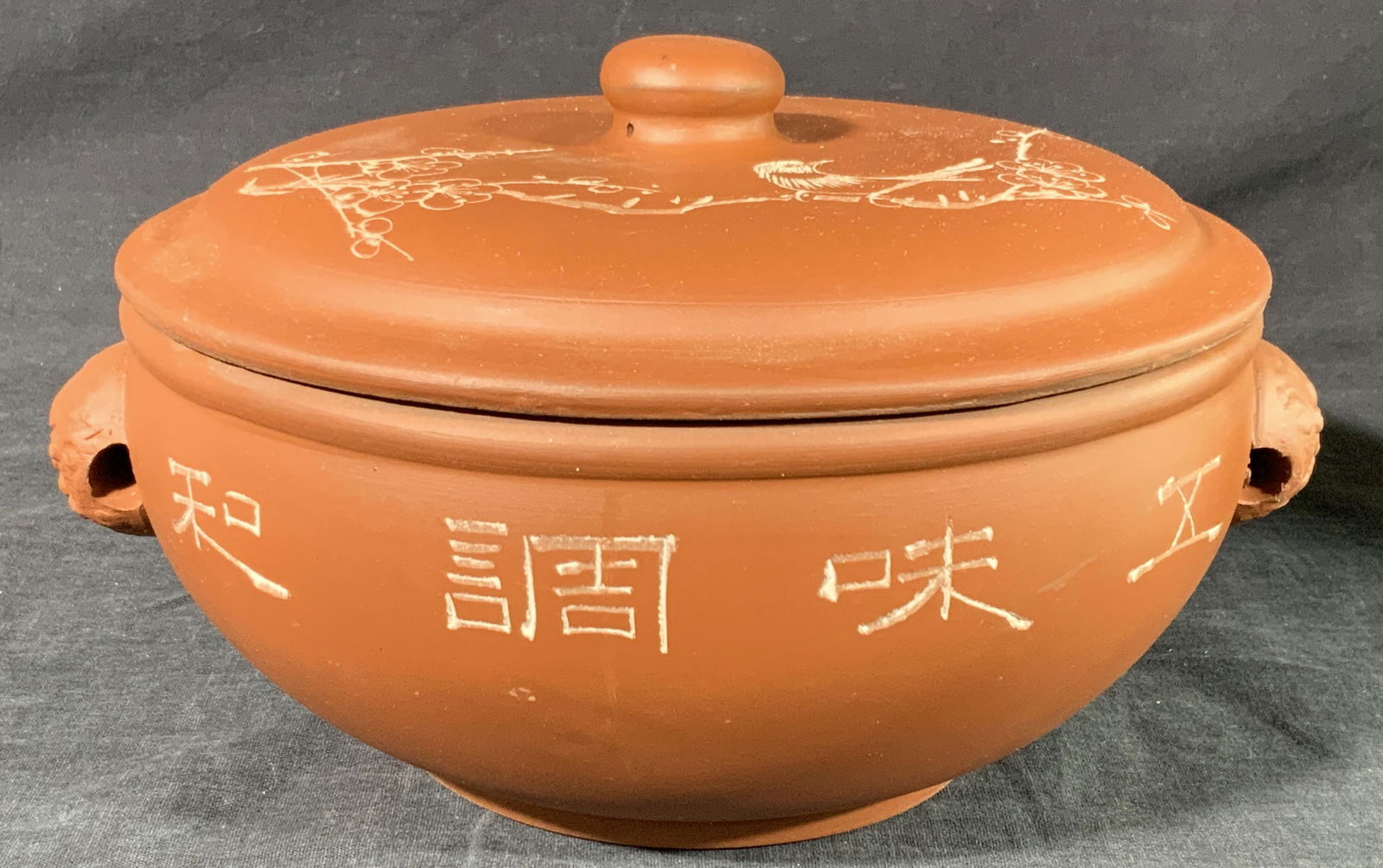 Vintage Asian Etched Zisha Clay Warmer Pot: A vintage zisha clay warmer pot with lid and handles with etchings of Chinese characters on body of pot and etchings of a bird on a branch of blooming flowers. Handles are formed to resemble guardian