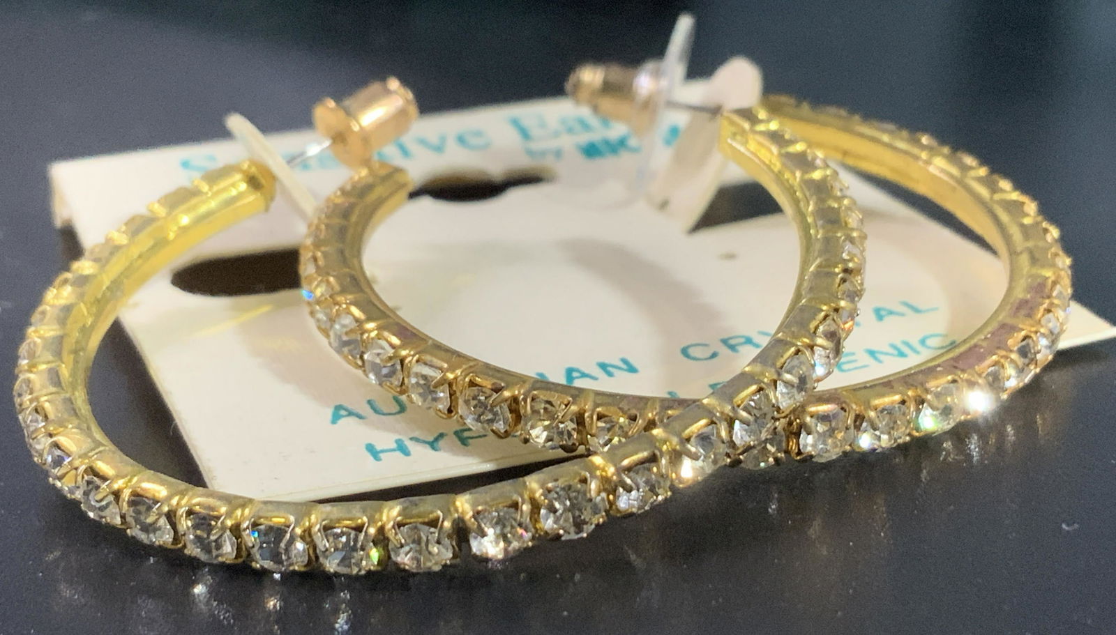 Austrian Crystal Hoop Fashion Earrings: A pair of gold tone metal 1.5 in. Hoop fashion earring with clear Austrian Crystals, prong set, Post backings for pierced ears. Thin but bold statement . Marked for Sensitive ears. Property of Manhatt