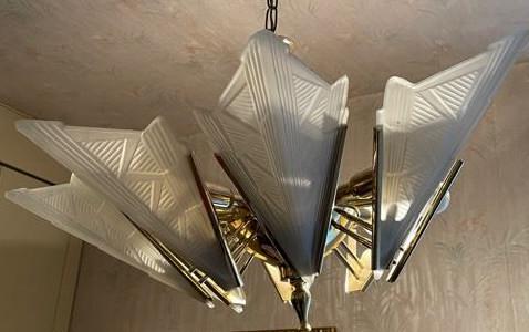 Art Deco Style Frosted Glass Chandelier: A vintage Art Deco style chandelier crafted from brass toned metal and accented with frosted glass. Geometric frosted glass features raised details. Eight arms. Measures approx. 28 inch drop x 25 widt