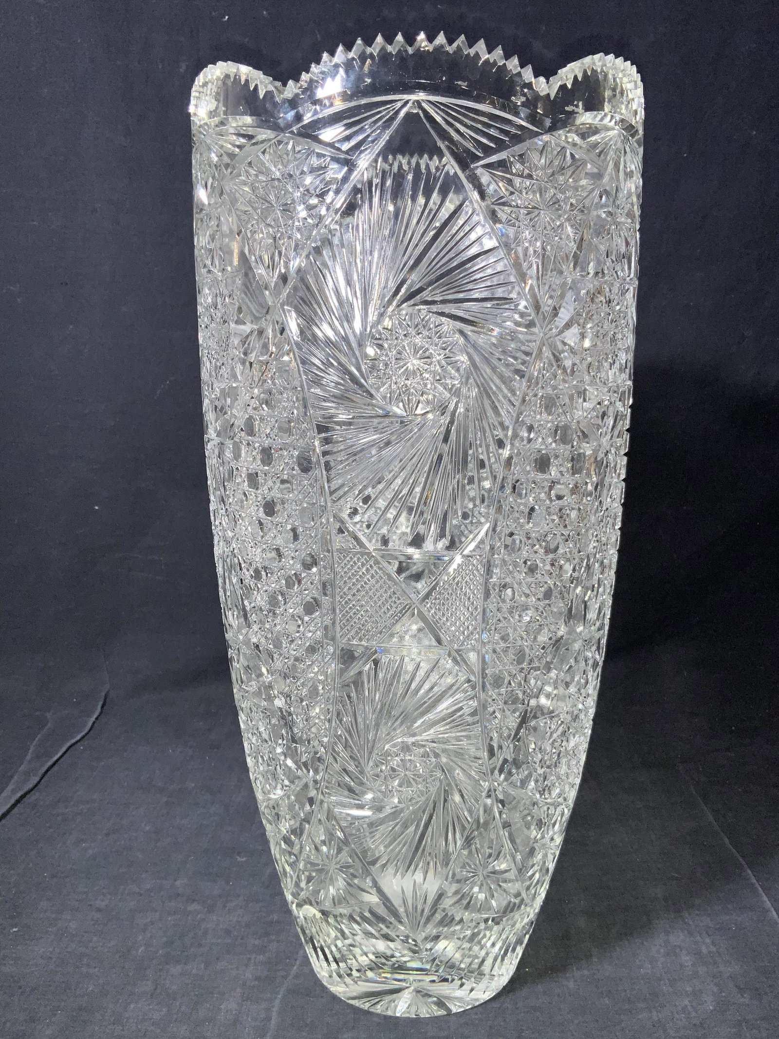 15 Inch Hand Cut Crystal Vase: A hand cut Crystal vase with saw tooth rims and multi cut sections that resemble stars, along with large over arching grooves separating patterns throughout vase. Approximately 15 inches tall. Some re