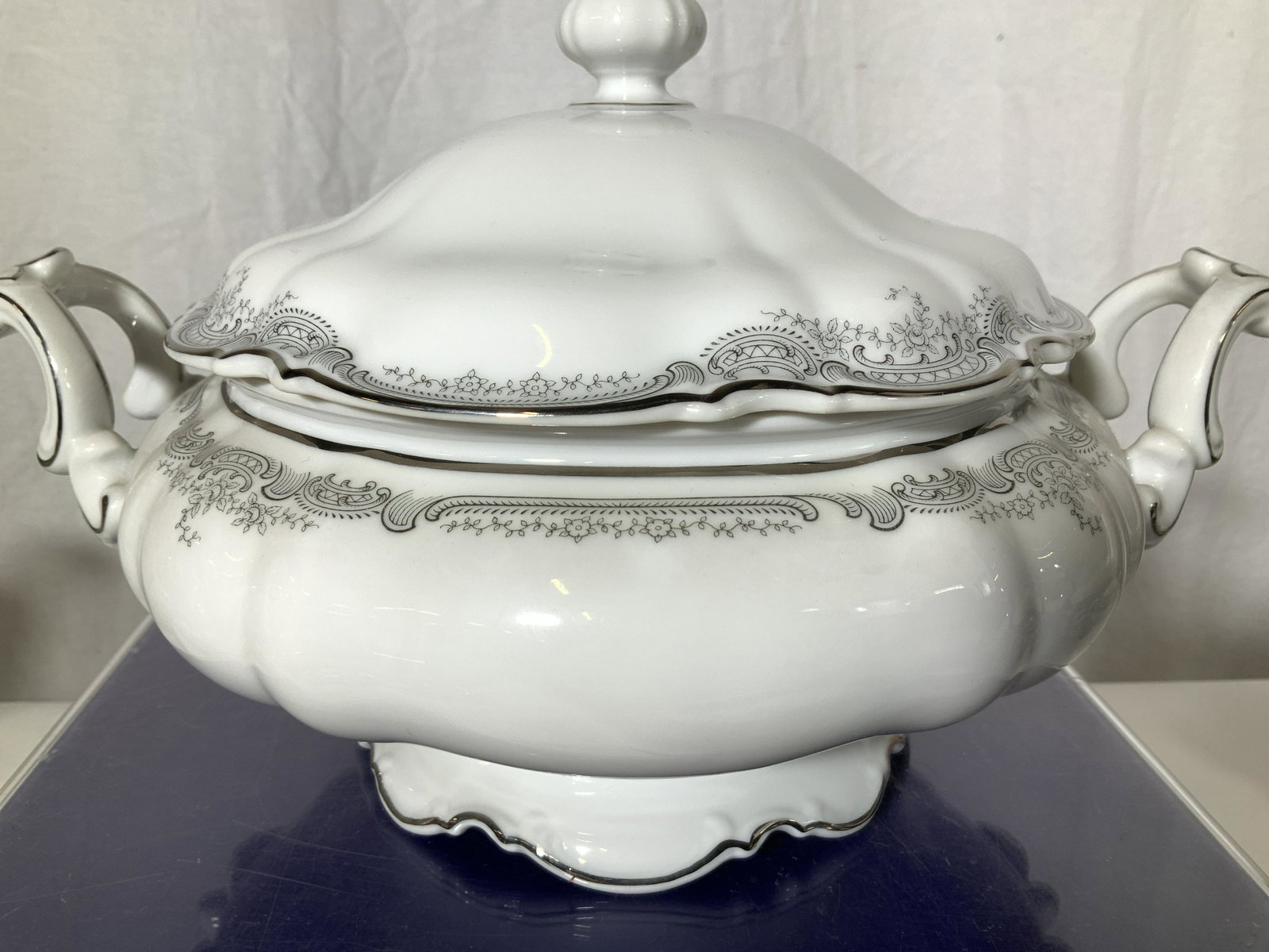 HUTSCHENREUTHER SYLVIA Porcelain Lidded Tureen: Fine Bone Bavarian China- Lidded tureen with side handles, white porcelain with grey scroll edge decor and silver plate rim. Scalloped edges. Tureen measures 12 in. total width, 4 in. Deep, 7.5 in. To