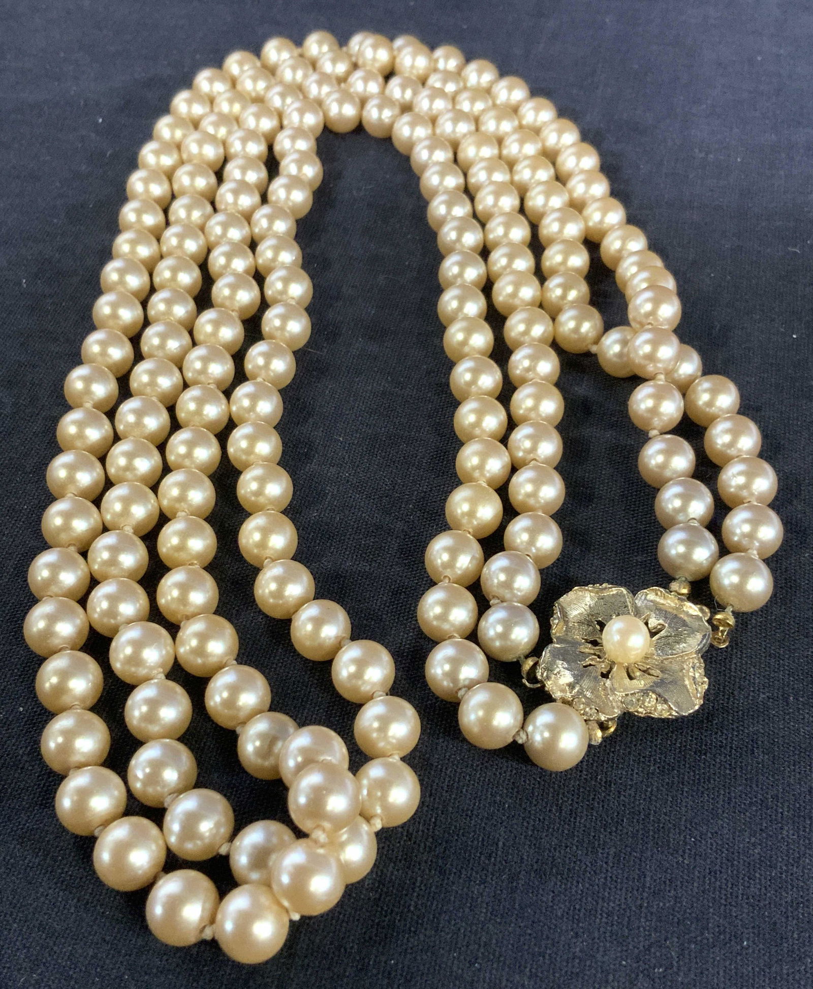 Champagne Toned Glass Pearl Necklace: Double Strand Necklace of glass pearls in champagne color with gold tone flower clasp with center pearl. Pearls measure 7 mm. Weighted piece, 26 in. Long. Beaded necklace, costume Pearl necklace, doub
