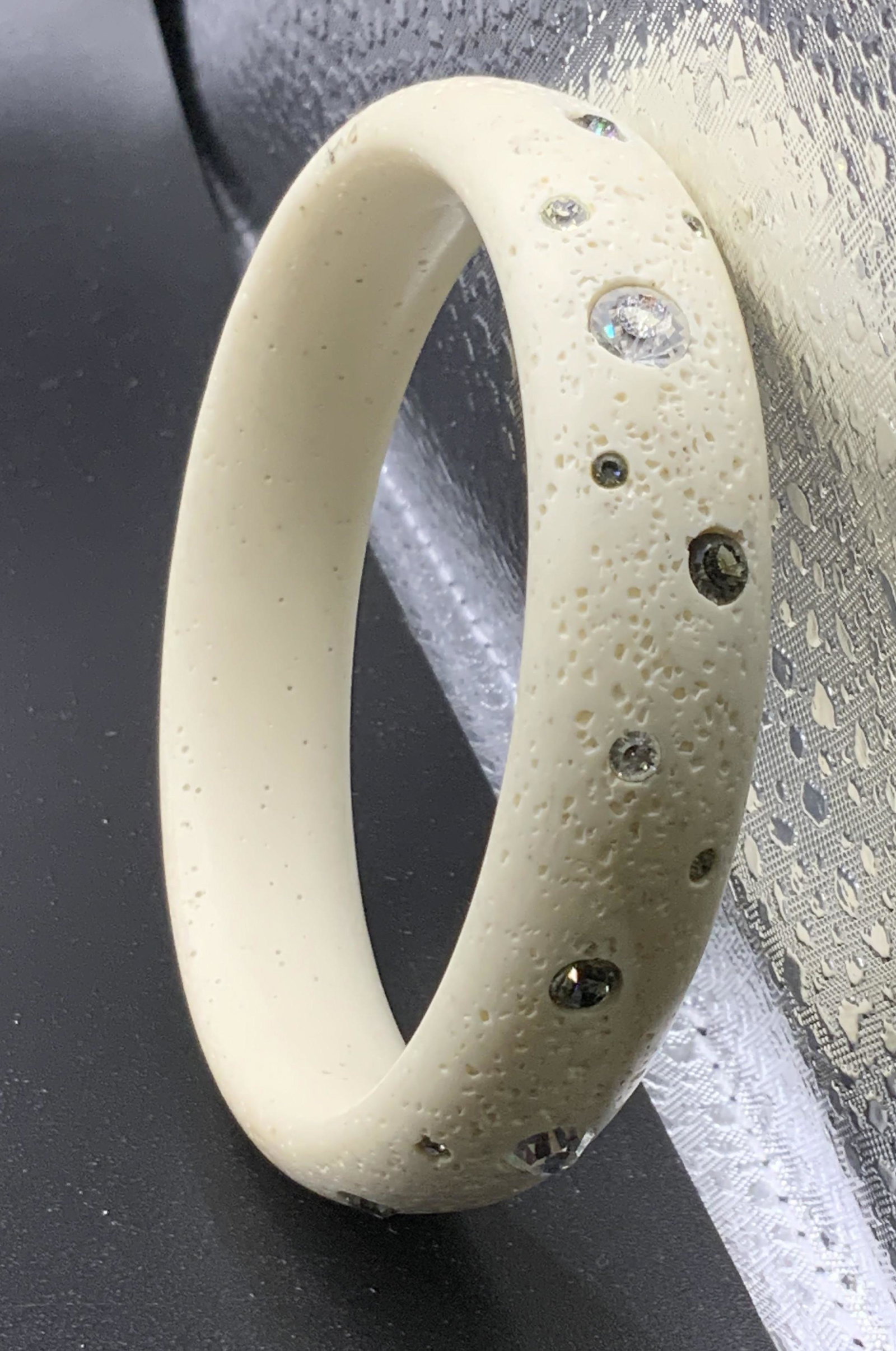 Floating Crystal Bangle Bracelet: Off white composite bangle, textured to resemble sandstone. Individual striking crystals places all around the bangle, floating in a minimalist pattern. Bangle width 5/8 in. Bangle diameter 2.5 in. Pr