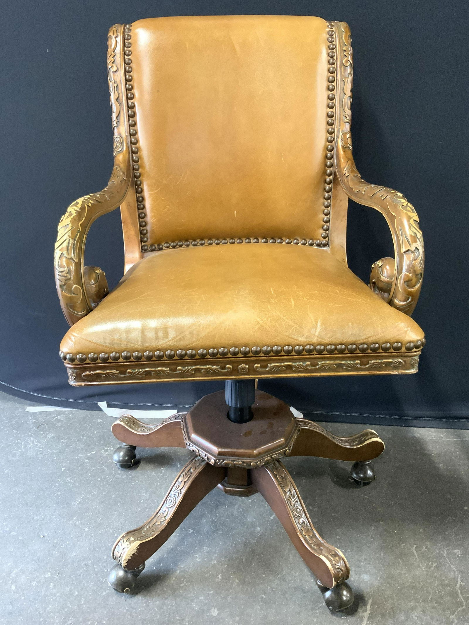 Vtg HOOKER FURNITURE Carved Wood Office Chair: Underside has tag which reads HOOKER FURNITURE. Piece has carved wooden floral, leaf & scroll detail around frame. Chair sits on 5 wheels. Backrest and seat are upholstered with beige toned leather wi