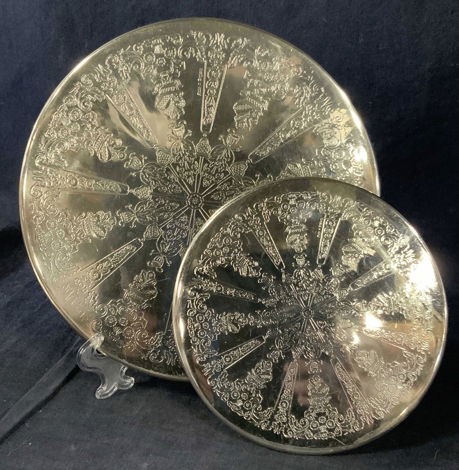 2 Etched White Metal Table Coasters: A group lot of 2 tabletop wine bottle coasters, made of a thin etched white metal with etchings of floral and fruit motifs. Undersides have green protective table felt. 2 varying sizes. Property of Ma