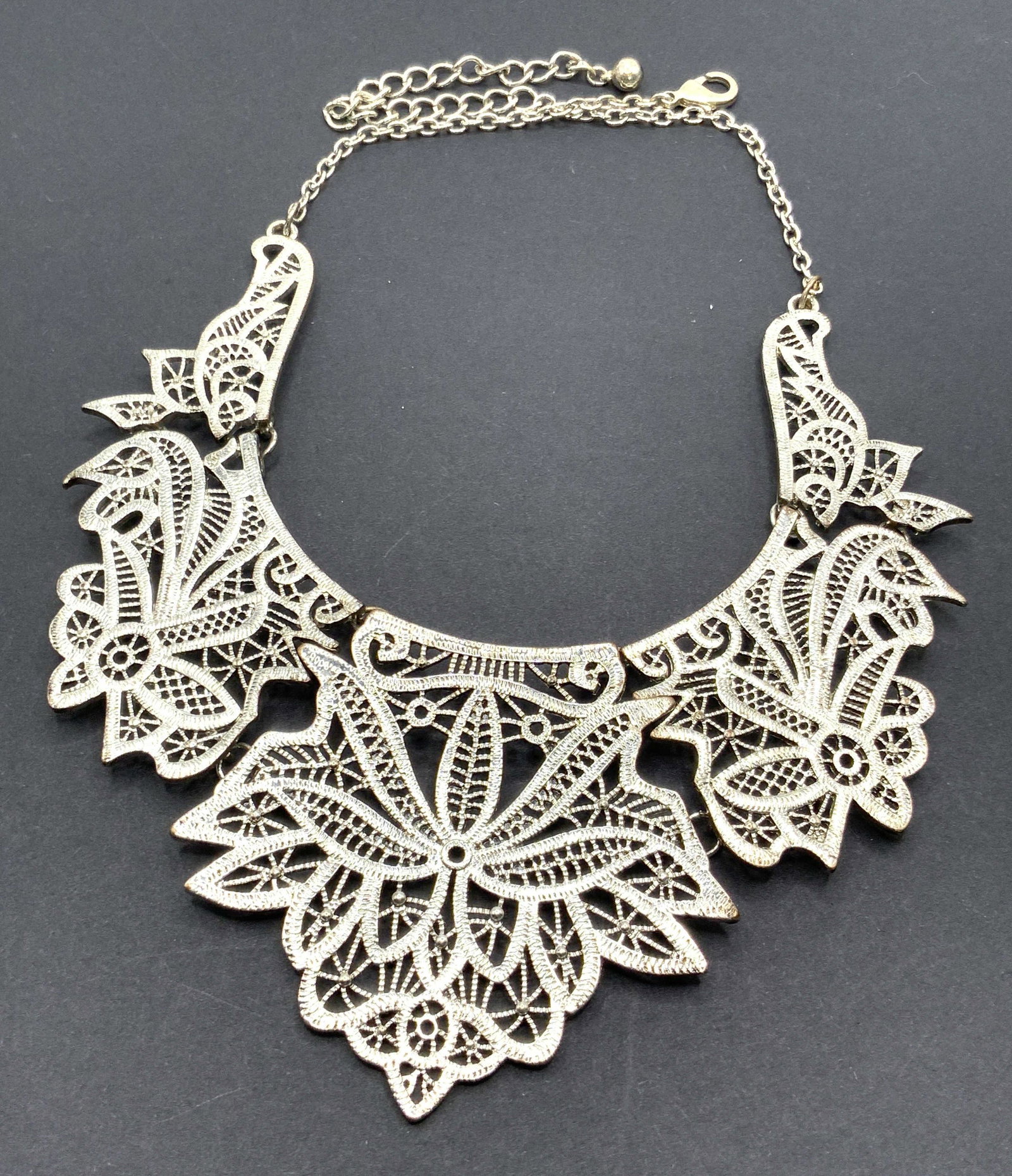 Vintage Pierced Filigree Metal Collar Necklace: A vintage pierced silver tone metal filigree bib style collar / choker necklace. Lobster claw clasp closure. Necklace length approx 17.5 in. Adjustable length. Some surface wear consistent with use an