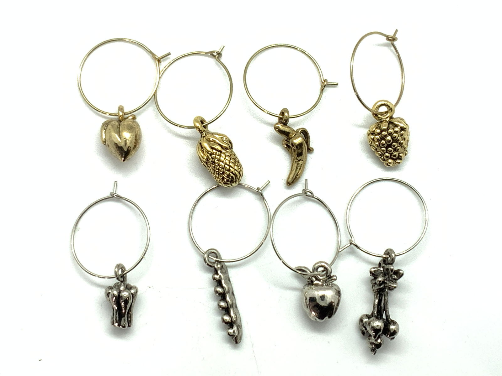 8 Wine Glass Charms: A lot 8 wine glass charms, 4 gold toned and 4 silver toned, all with fruit or vegetable charms, ranging from pineapples, pea pods, peppers, peachs, bananas, strawberries, etc. Hoops are approximately