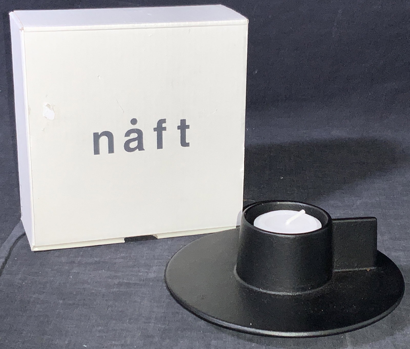 NAFT T DEMI+ Modern Metal Candle Holder W Box: A modern style black metal candle holder by NAFT, in original box. Holder has a flat base with a section to place a tea light with extension for holder. Marked NAFT on underside. Box is marked NAFT. H