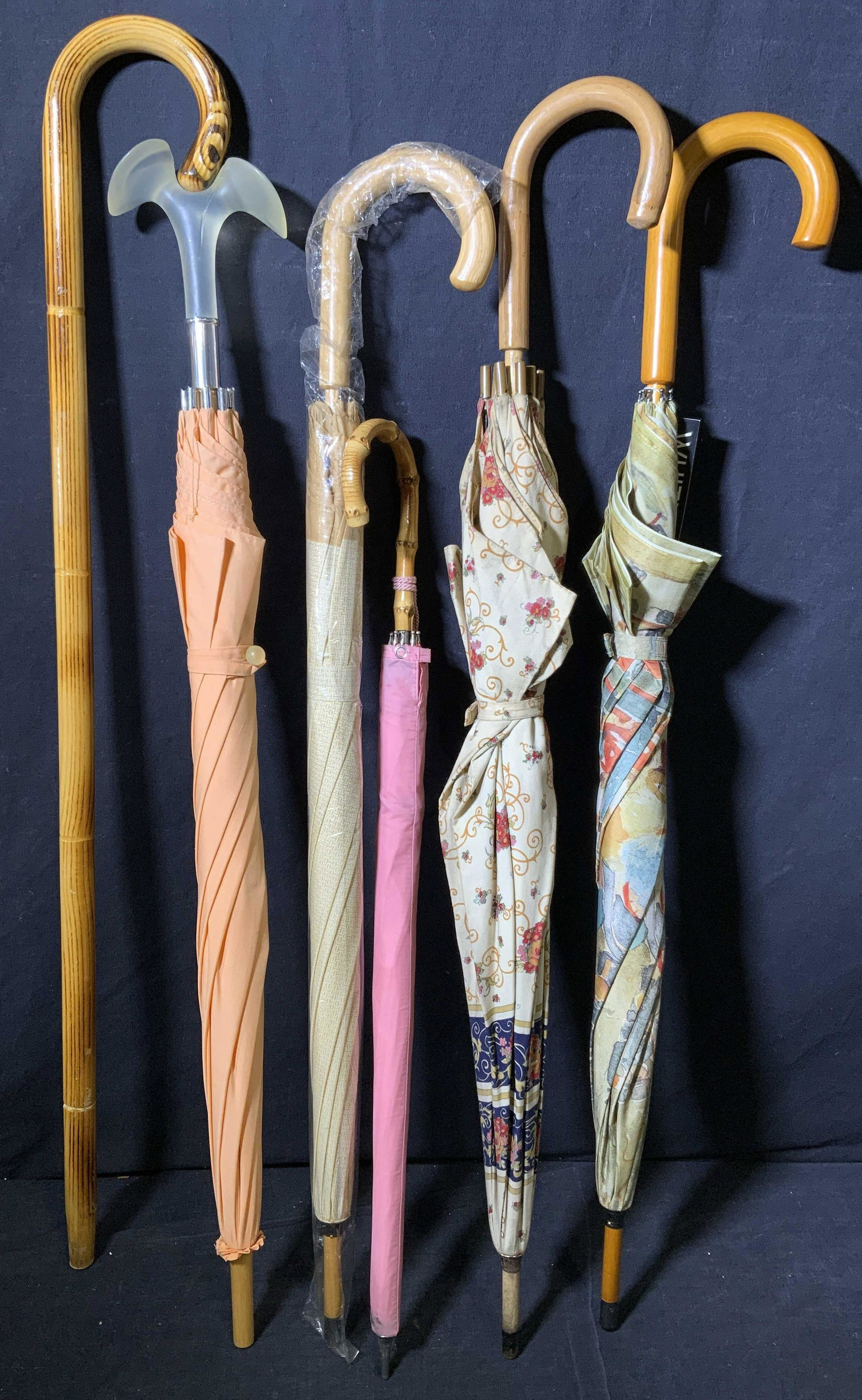 Group Lot 6 Umbrellas & Other: Includes 5 umbrellas 1 wooden cane. Pieces are possibly vintage. Surface wear present, strap securing canopy on parasol is damaged. One umbrella marked Whitney Museum of American Art. Largest piece me