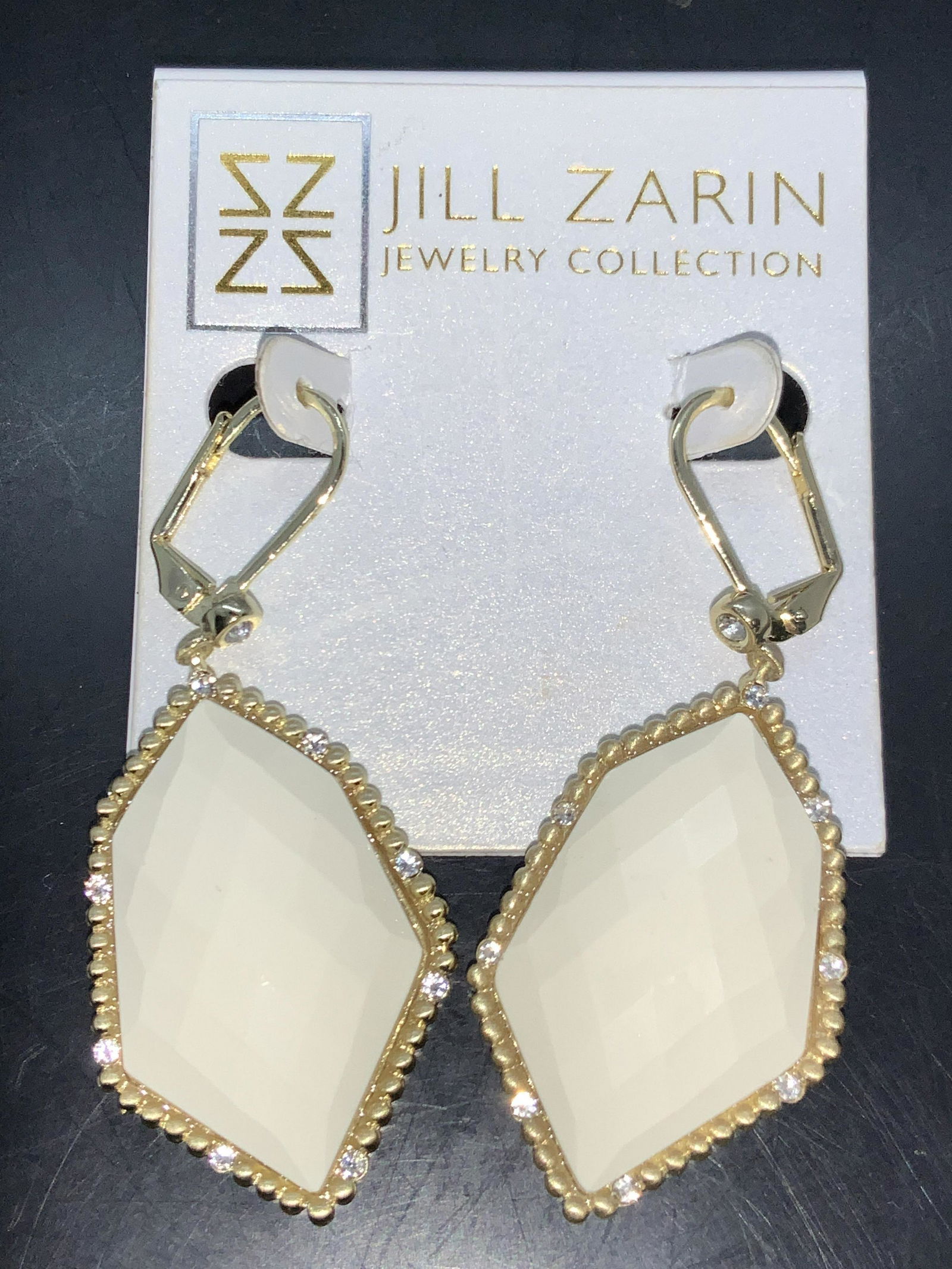 Jill Zarin Dangle Cocktail Earrings: Pair of gold toned dangle earrings with lever backs, with white faceted composite center stone with frame of faceted crystal accents. Comes on original store display card marked Jill Zarin Jewelry Col