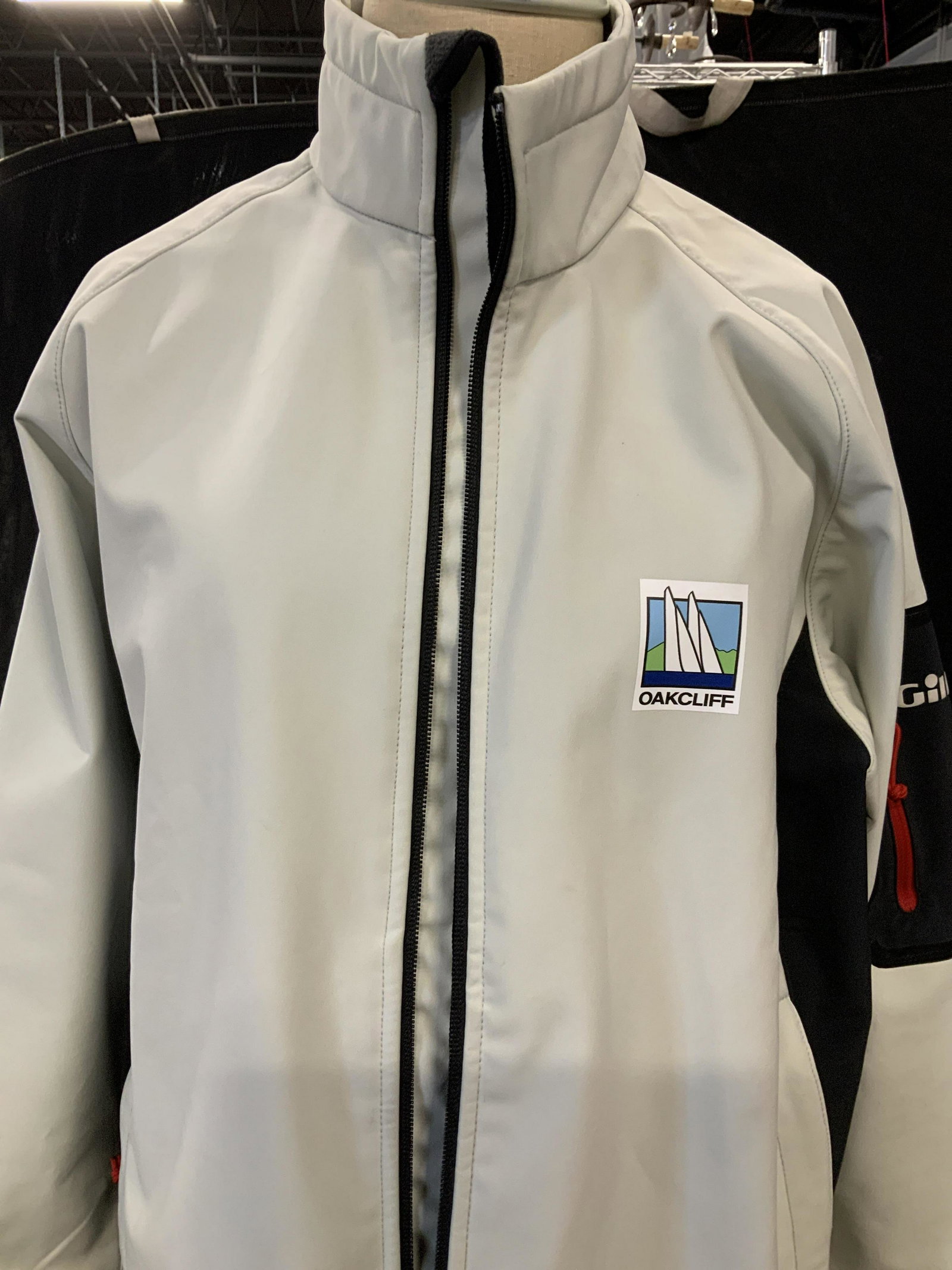 OAKCLIFF WINDPRROF WATERPROOF JACKET: Polyester OACKCLIFF Racing jacket by designer Gill, black fleece interior lining. sportswear that is waterproof, windproof, and warm. Light grey color Size Medium. Zippered Hand pockets and sleeve poc