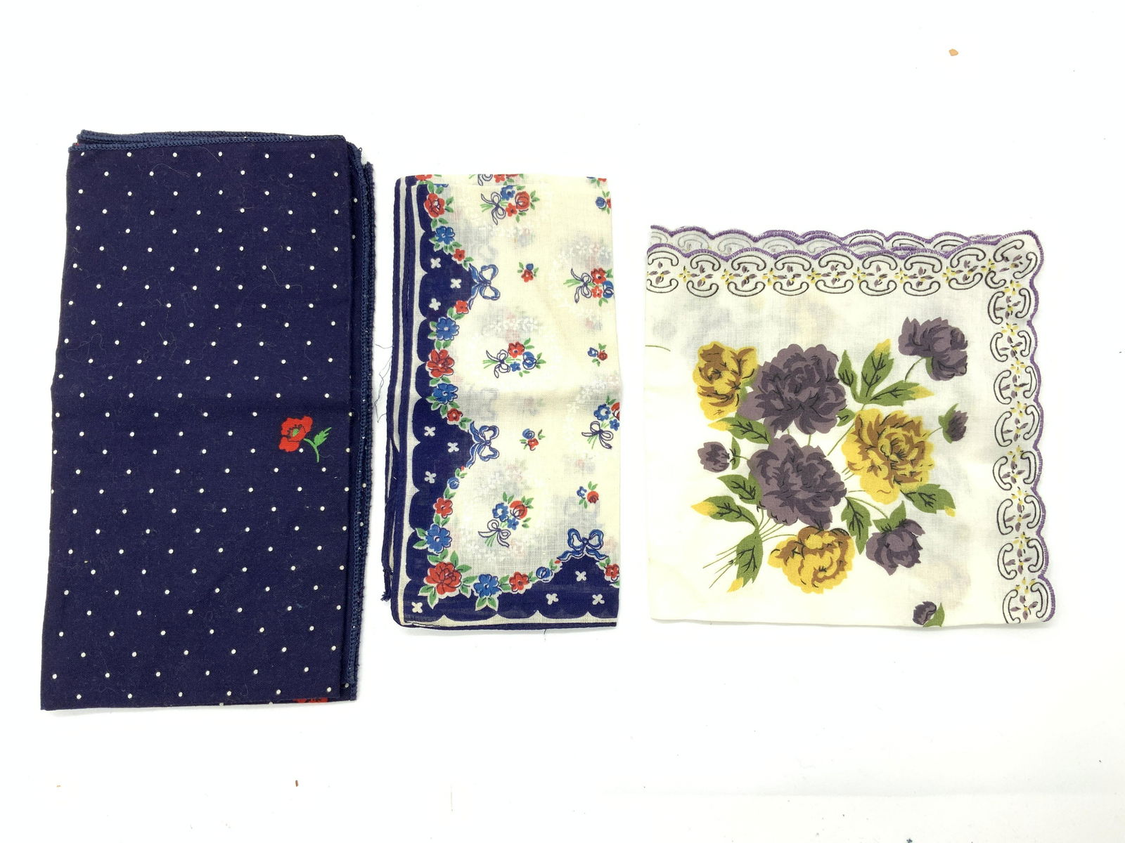 3 Vintage Floral Handkerchief: A group lot of 3 floral handkerchiefs. 1 cream toned with purple threaded edges with purple and yellow flowers. 1 royal blue edged handkerchief with red and blue flower motifs with red ribbons. 1 roya