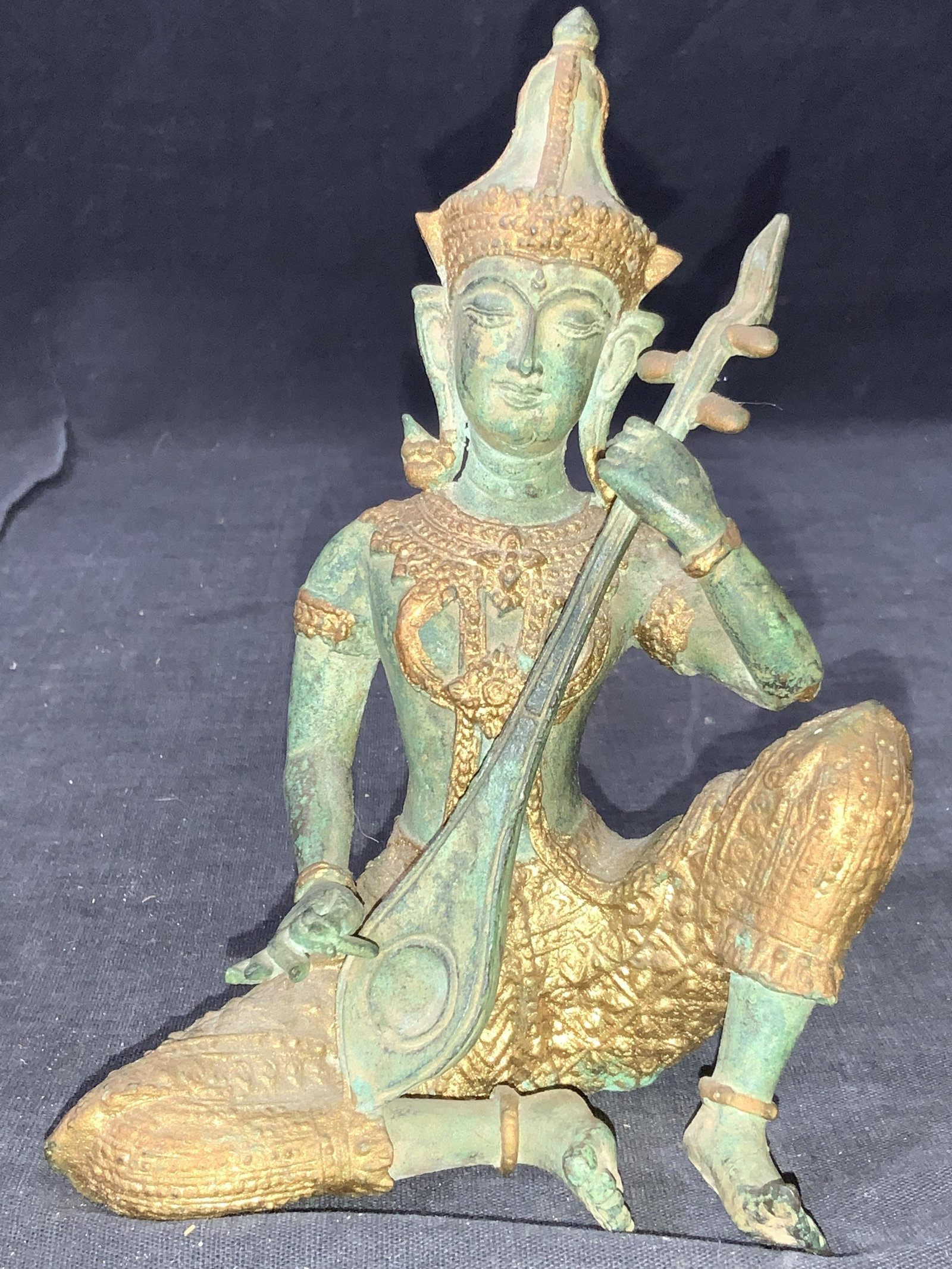 Asian Prince Cast Bronze Figural W Instrument: A cast bronze Figural of a Thai prince playing a guitar like instrument. Body of the figure has a sea green tone with clothing and jewelry and head piece being a gold toned metal. Approximately 6.5 in