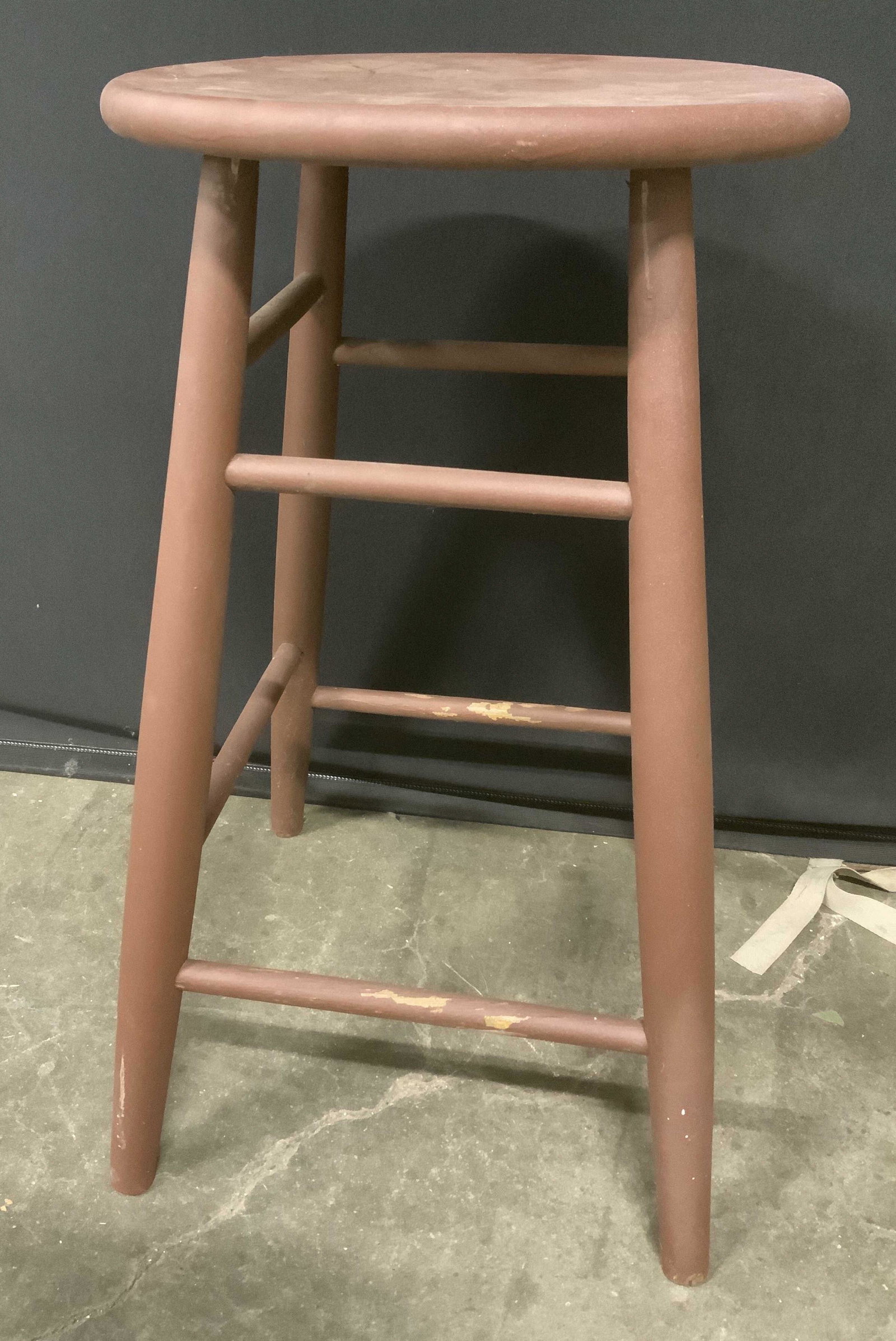 Vintage Wooden Stool: Vintage wooden stool. Colored maroon toned. Legs joined by four horizontal stretchers. 24 inches h and 14 inches in diameter. Chipping to paint present. Home decor, decorative accessories, decorative 