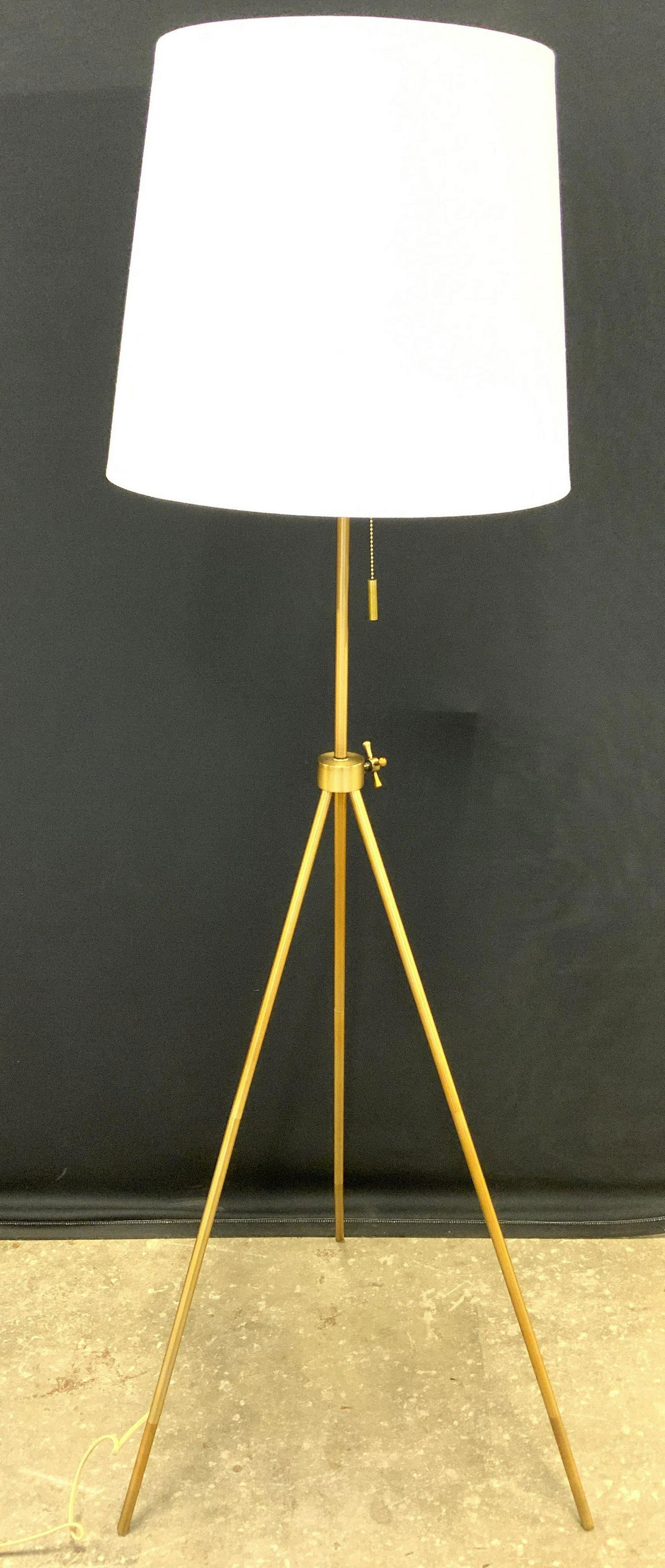 MASTERCRAFT INTL Metal Tripod Floor Lamp W Shade: Tag on lamp wire reads MASTERCRAFT INTERNATIONAL. Lamp is gold toned and appears to be brushed metal. Piece includes white toned shade & gold toned cylindrical shaped finial. Piece has dangling pull s
