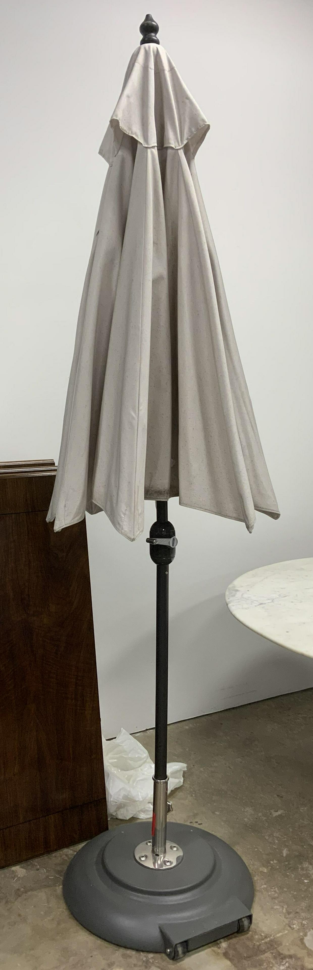 TUCCI Outdoor Patio Umbrella: Base is trademarked TUCCI. Umbrella has cream toned canopy. Base of umbrella has 2 wheels & appears to be filled with cement for bracing. Measures approx 105 inches tall & wide when fully open. Umbrel