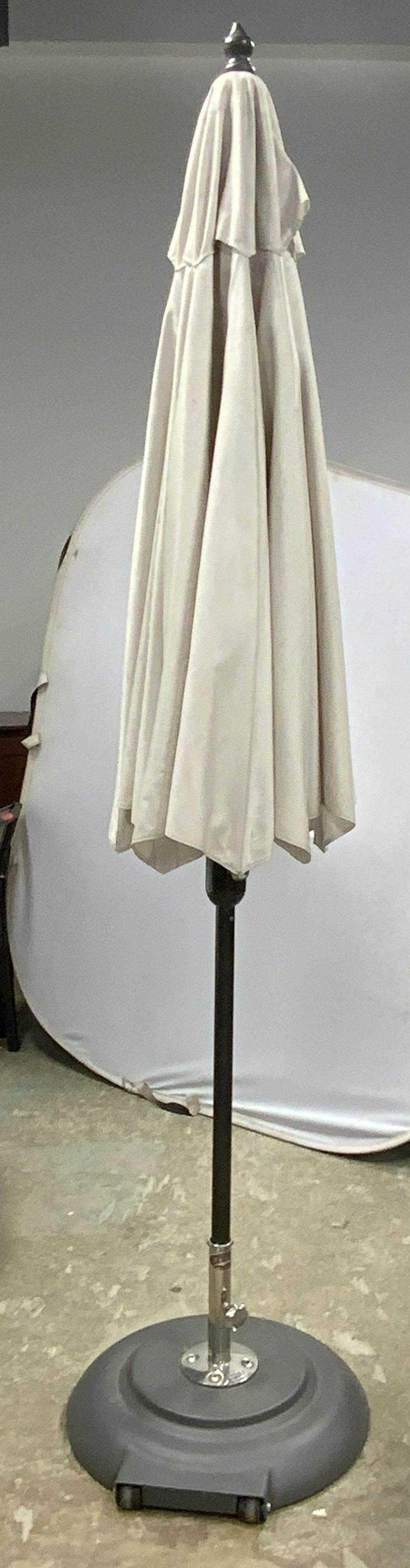 TUCCI Outdoor Patio Umbrella: Base is trademarked TUCCI. Umbrella has cream toned canopy. Base of umbrella has 2 wheels & appears to be filled with cement for bracing. Measures approx 105 inches tall & wide when fully open. Umbrel