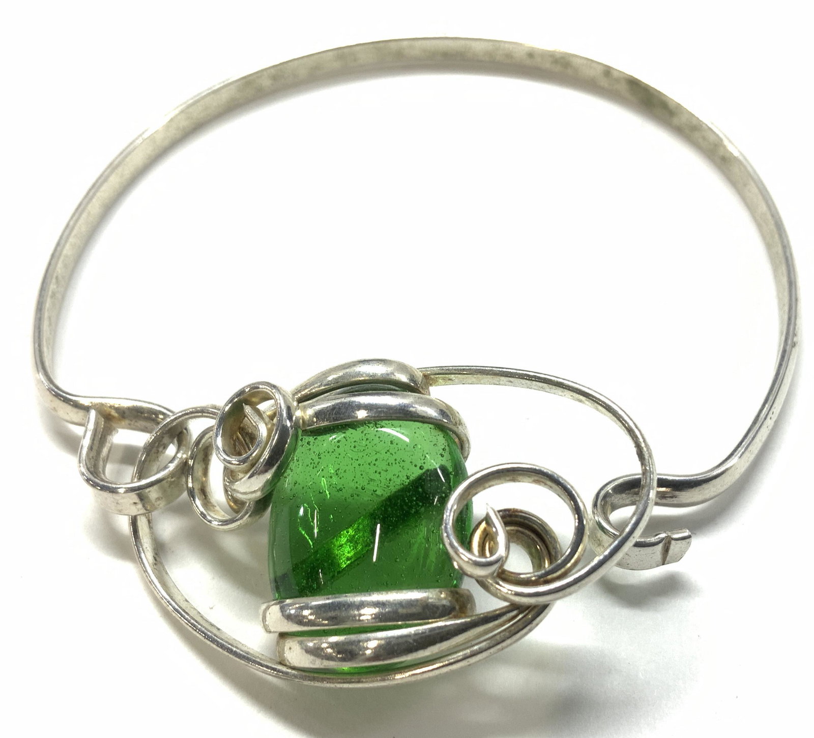 Artisanal Green Glass Bead Bracelet: Silver tone metal bracelet with center green glass stone wrapped in metal with swirl design. Hook and loop closure. Stone measures 5/8 in. App 2.5 in. diameter. Glass jewelry, artisanal bracelet, hand