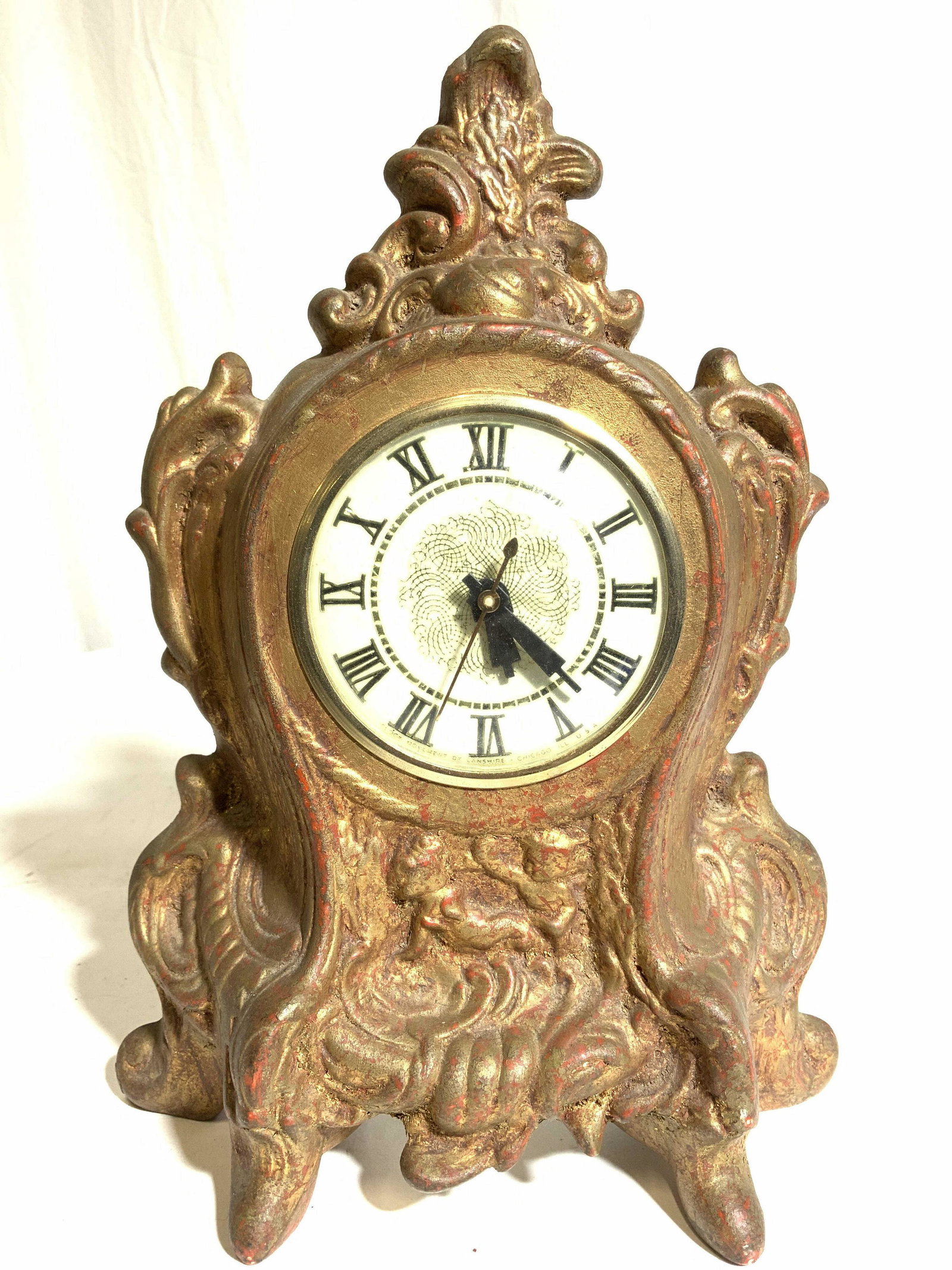 Vntg LANSHIRE Ornate Gilded Mantel Clock: Clock face reads LANSHIRE. Piece is ornately detailed and covered in gold leaf. Clock appears to be metal, possibly porcelain, possibly composite. Clock face is circular shape with cream toned face an
