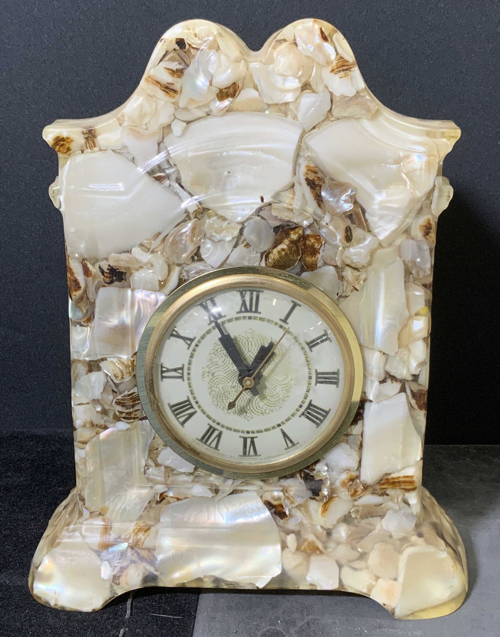 Vintage Mother of Pearl Clock: Vintage clock, electric clock. Crafted from mother of Pearl suspended wishing a composite material, possibly resin. Label on back reads as Handcrafted Authentic Mother of Pearl, back of clock reads as
