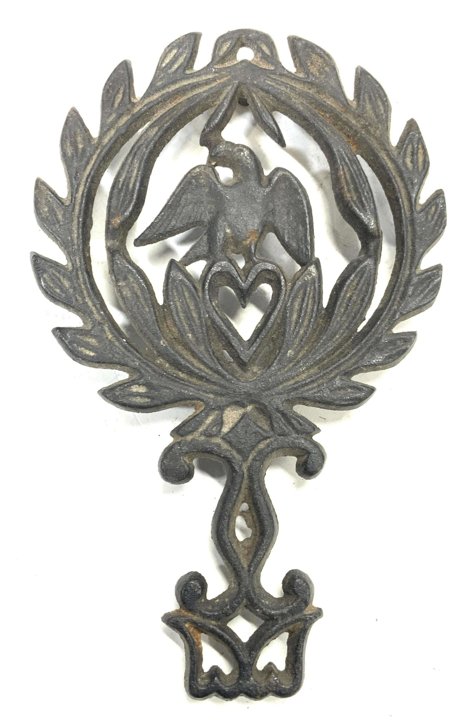 Vintage Iron Kitchen Trivet: A vintage iron made trivet with leaf like exterior patterns with interior pattern consisting of a heart with a bird perched atop the heart. Approximately 8.25 inches long and 5 inches wide. Condition 