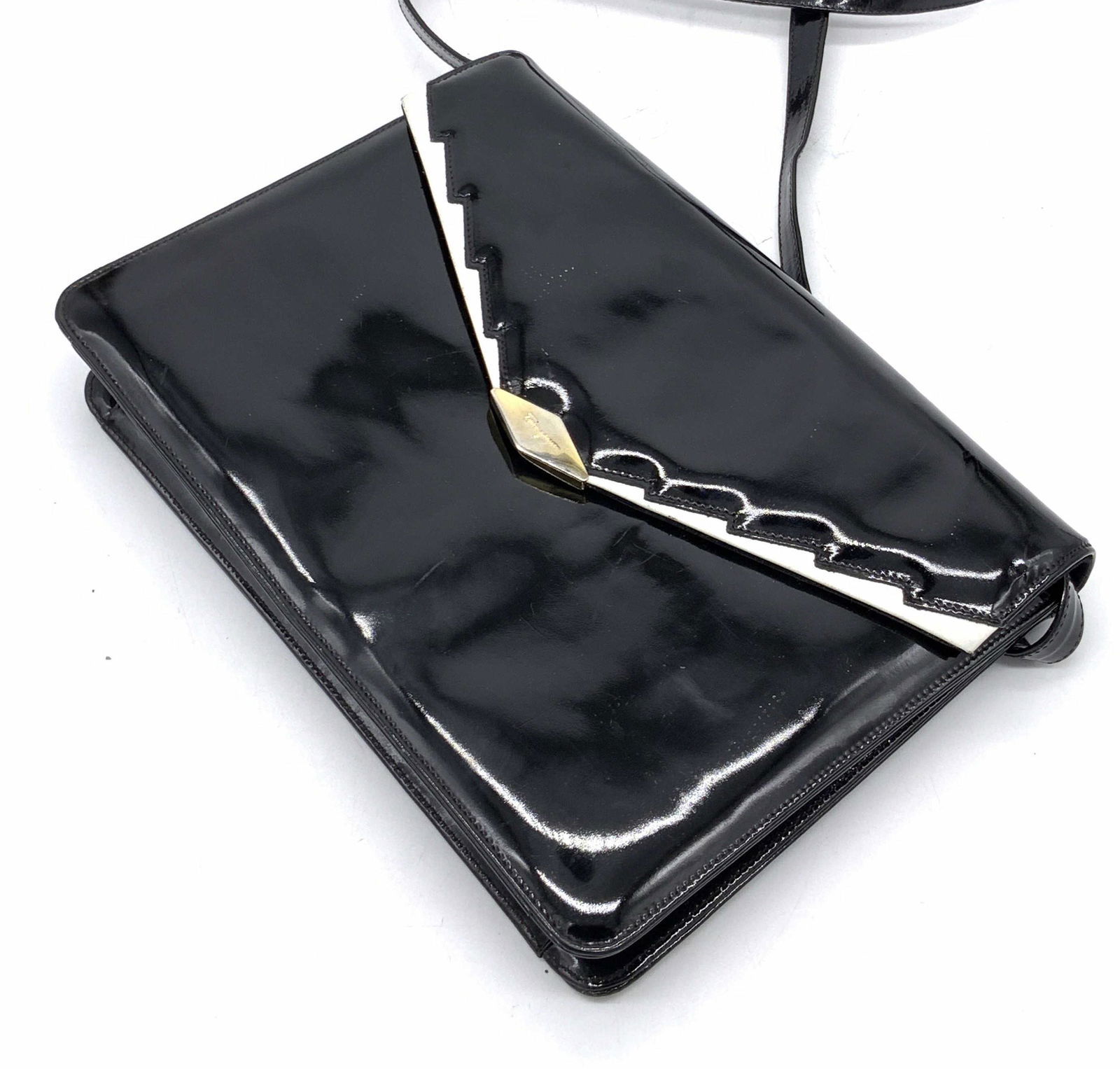 SALVATORE FERRAGAMO Italian Patent Leather Purse: A black patent leather purse with white accents and gold tone hardware. Obverse reads FERRAGAMO. Interior signed SALVATORE FERRAGAMO, made in Italy. Zipper pocket to interior. Strap drop approx 13 in.