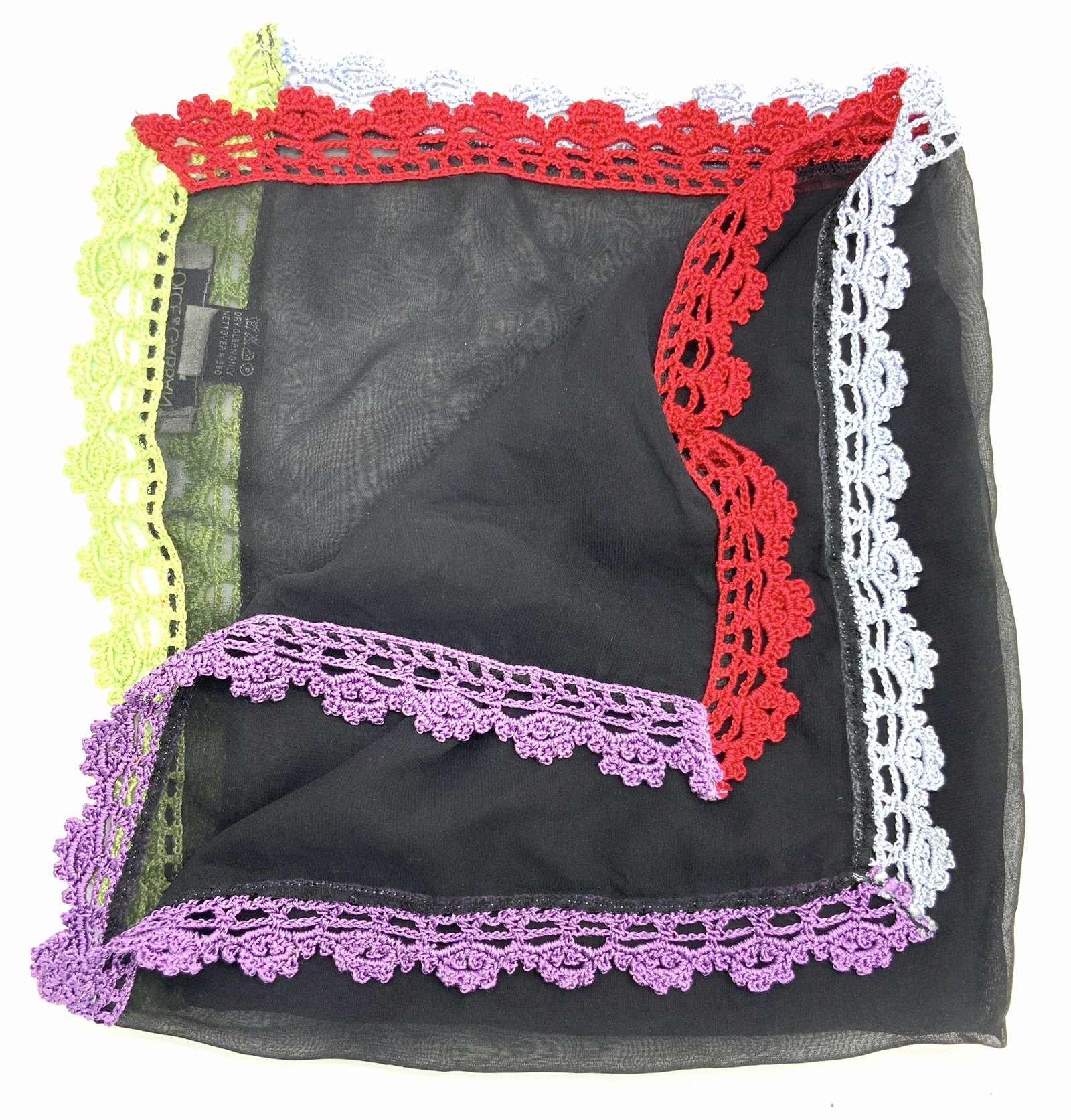 DOLCE & GABBANA Silk Crochet Sheer Handkerchief: A silk handkerchief marked on tags Dolce & Gabbana Fourlards, Made in Italy, 100% Silk. Handkerchief is sheer black with intricate crocheted edges, made of varying colors such as red, blue, purple and