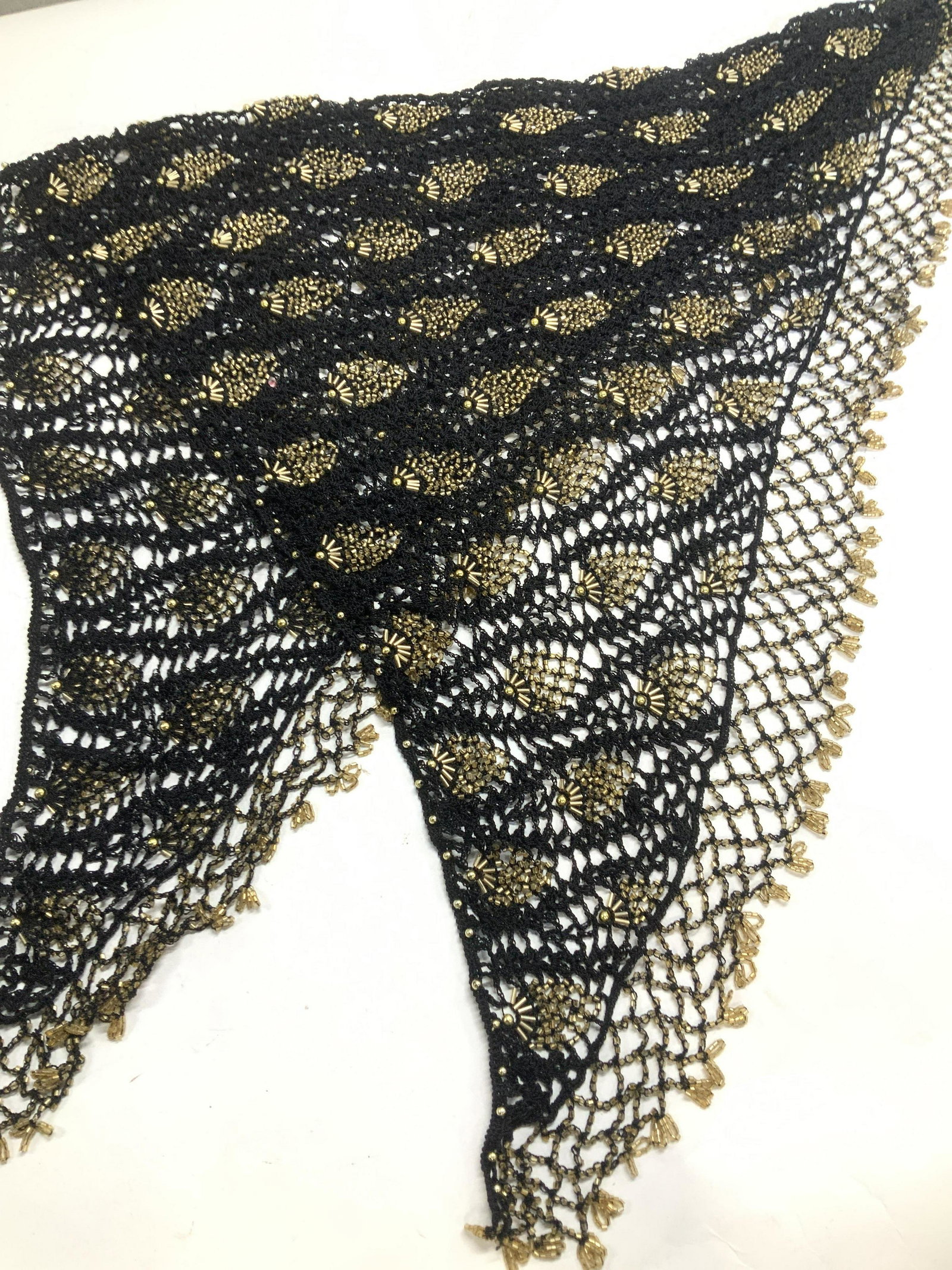 Hand Crafted Crochet Shawl/ Accessory, Hand Beaded: Black Crochet shawl , appears to be hand knit, with gold beading along hems. Peacock tail style pattern on body of shawl. In triangular shape. Measures 27 in. Long, 45 in. Wide. Up cycle into waist we