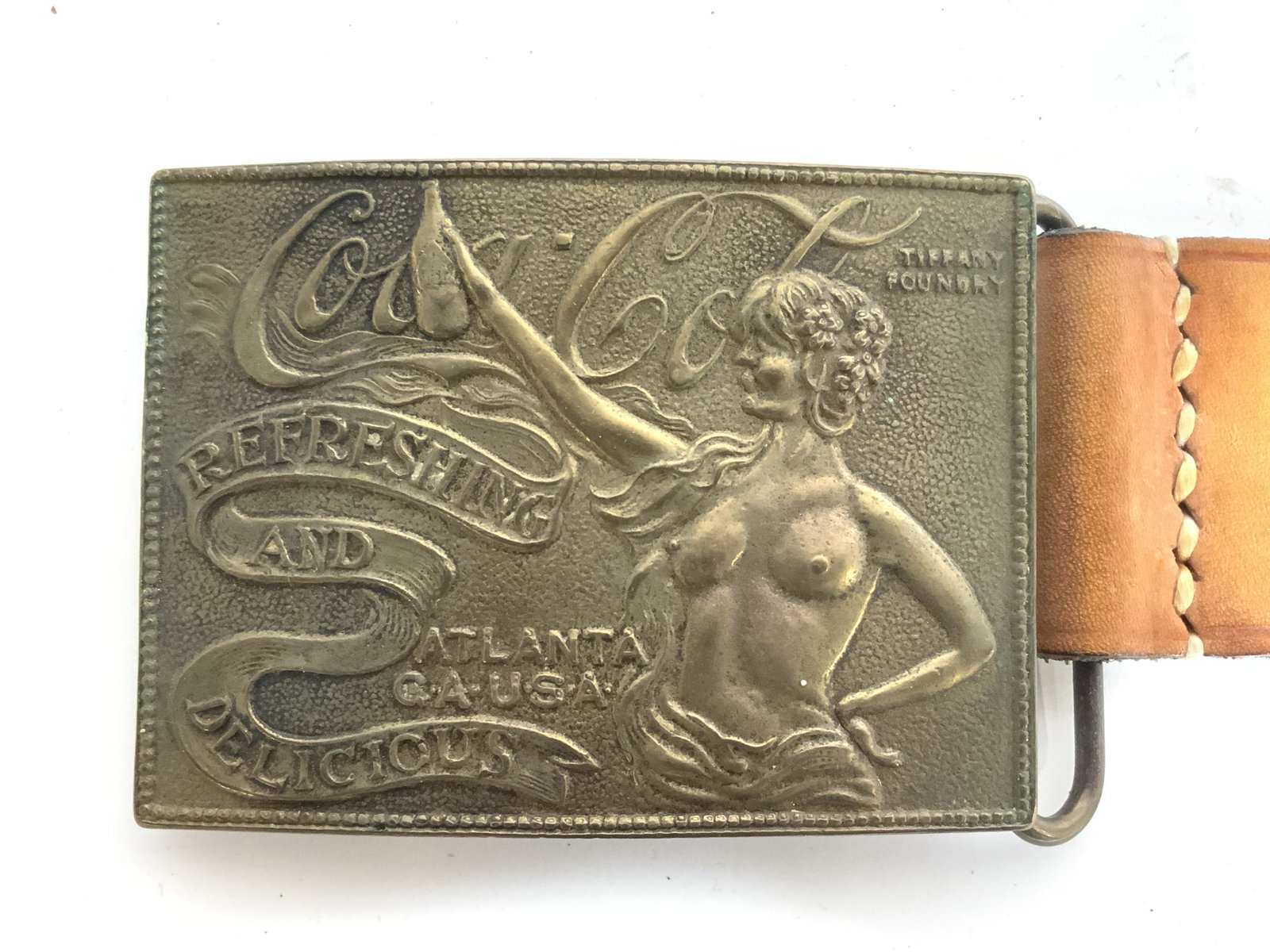 Leather Belt W COCA COLA Female Nude Buckle: Belt is beige toned and appears to be leather. Piece has brass buckle which reads COCA COLA and has female nude figure. Top left corner of buckle reads TIFFANY FOUNDRY. Belt measures approx 42 inches 