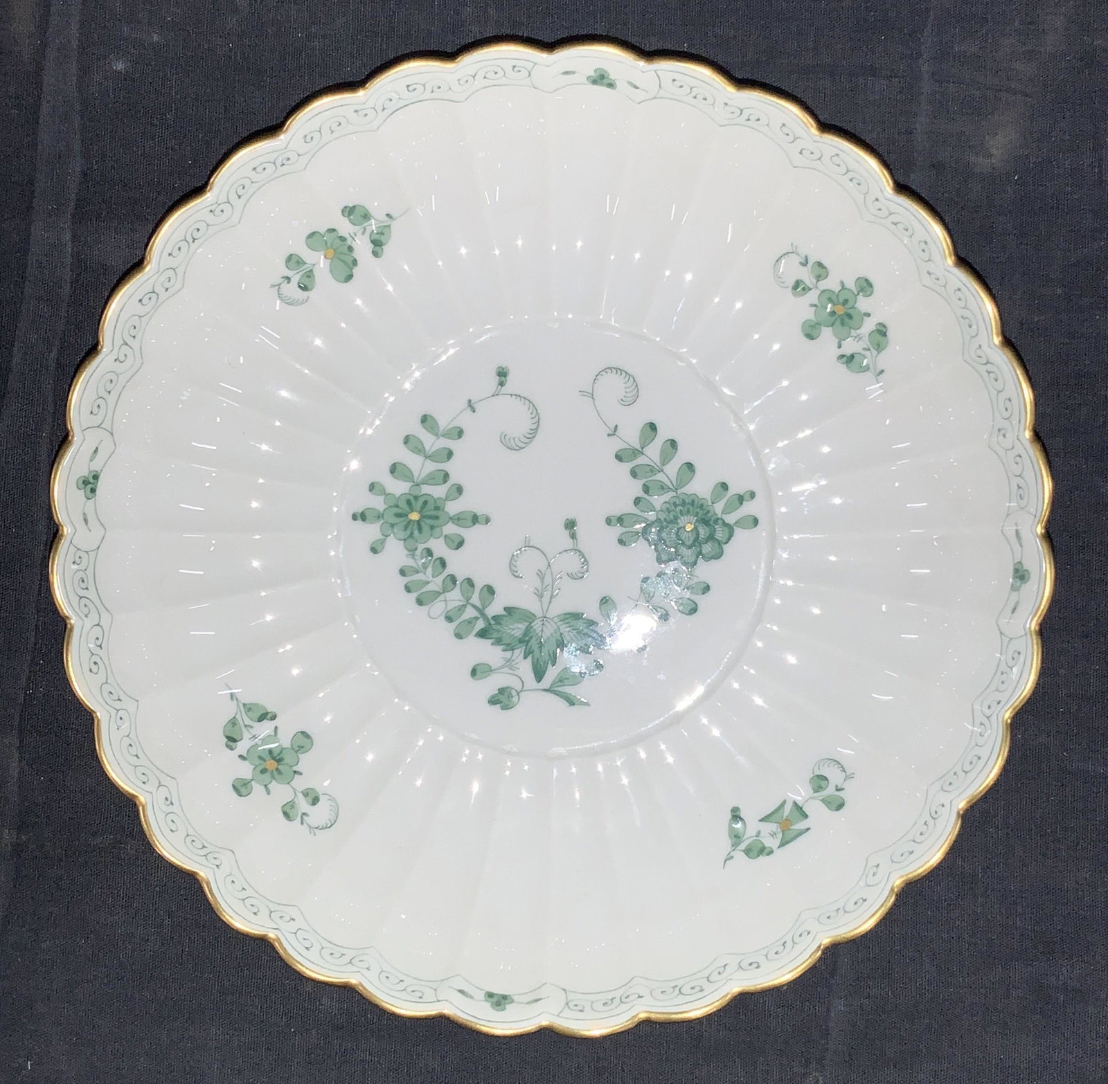 MEISSEN German Porcelain Shallow Bowl: A white porcelain shallow bowl with scalloped edges and gold gilt rims. Painted on interior with green spiral designs on edges and painted flowers in the center. Trademark to underside double crossed 