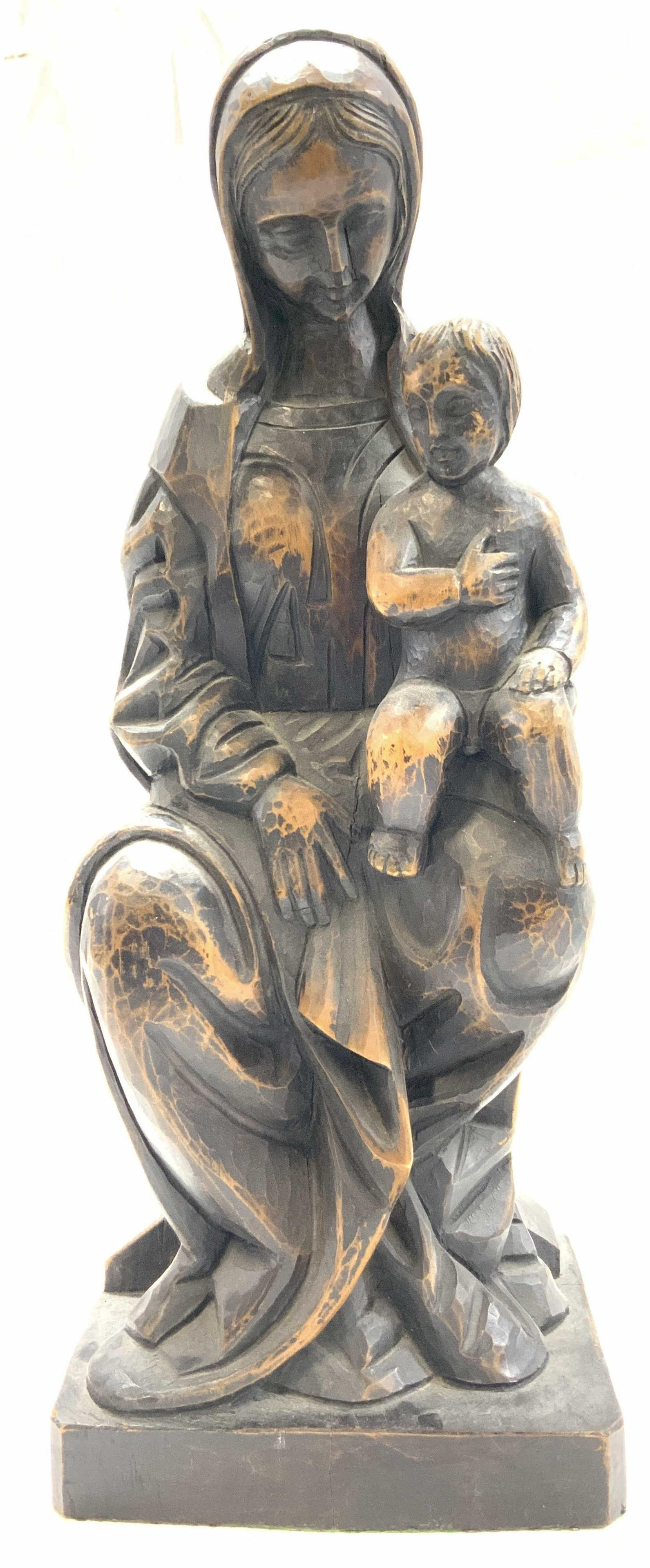 Carved Wooden Mary & Baby Jesus Statue: Carved wooden statue depicting the Mother Mary in robes and cowl, head positioned downward with the baby Jesus on her lap with a hand on his heart. Approximately 19.75 inches tall and 7 x 9 inches wid