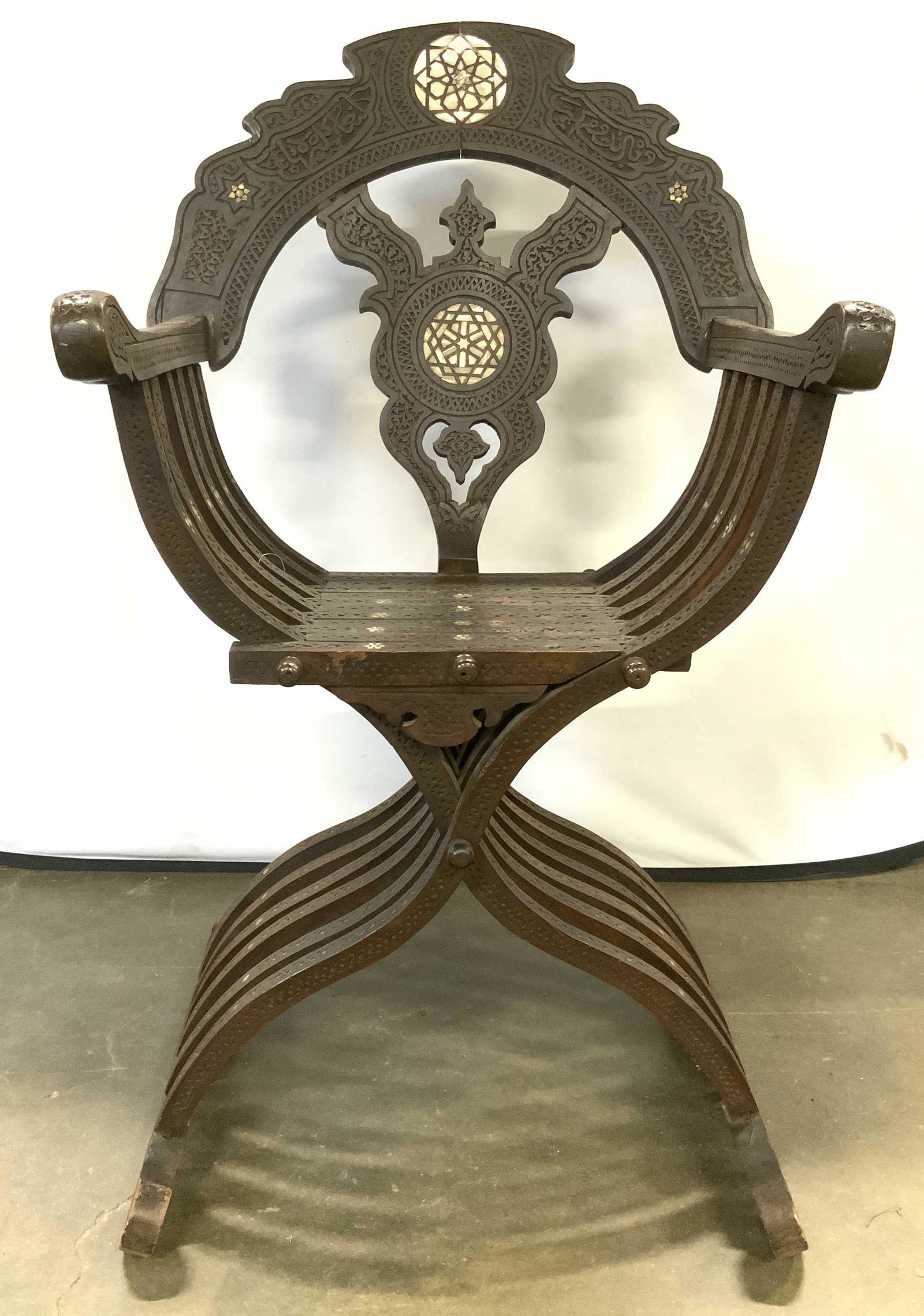 Antique Wooden Syrian Damascene Savonarola Chair: Savonarola chair is antique and ebony inlaid wood. Piece has intricately carved detail. Piece also has mother of Pearl inlay detail. Chair has curved wooden interlocking structures. Hand carved with i