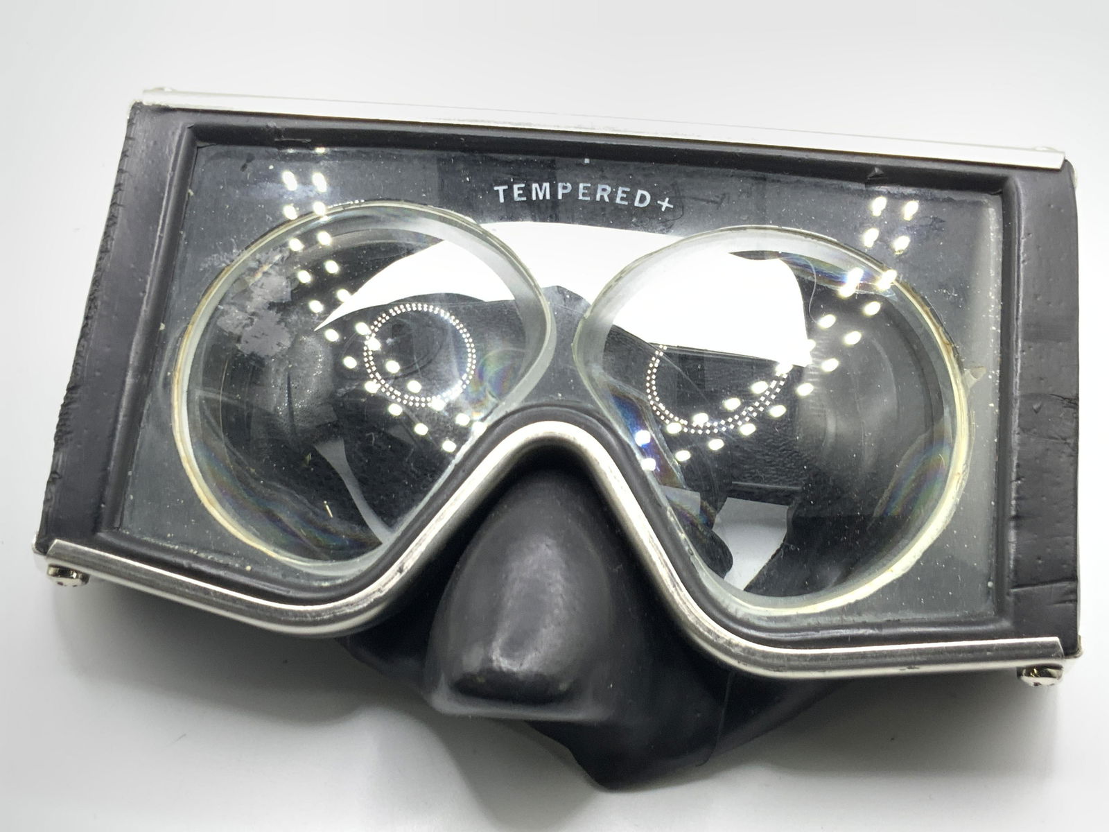 TEMPERED Glass & Rubber Goggles, USA: Goggles appear to be crafted from glass, metal, and rubber. Adjustable. Black and silver hues. Reads MADE IN USA, TEMPERED. Measures 3.5L x 8W in. Sone surface wear, some scratches. Goggles, TEMPERED