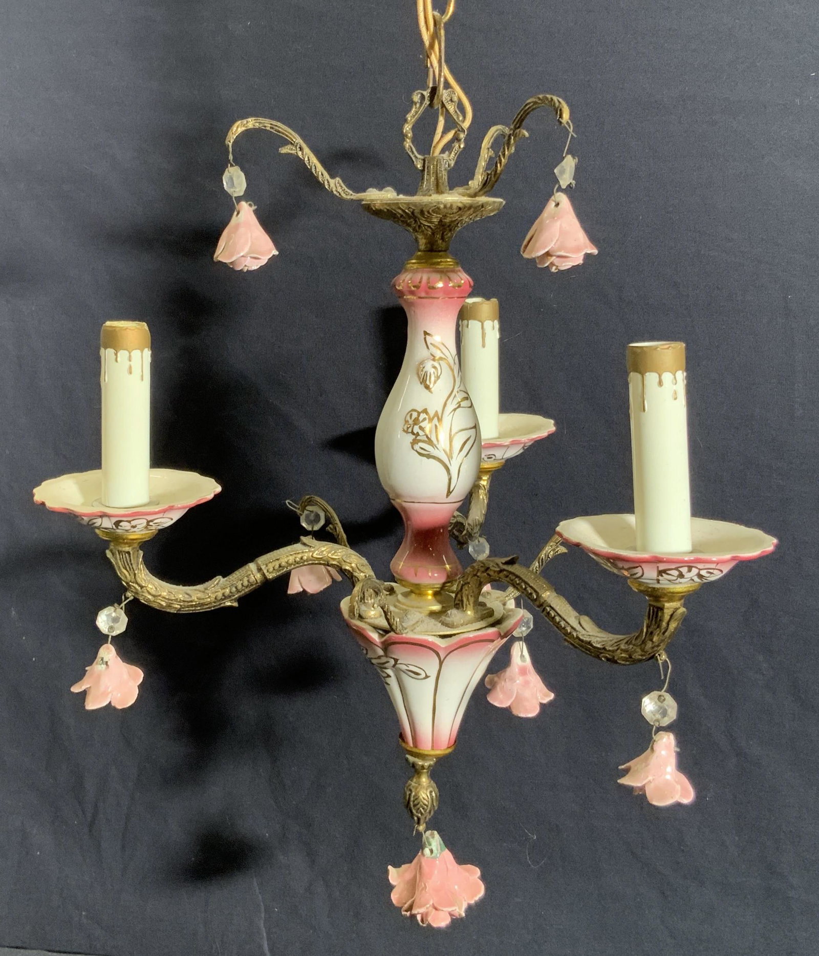 Vintage Hand Painted Porcelain Floral Chandelier: A hand painted porcelain three arm chandelier with etched metal hardware. The body of the chandelier is primarily pink and white hued with gilt accents. Dangling porcelain florals along the piece, two