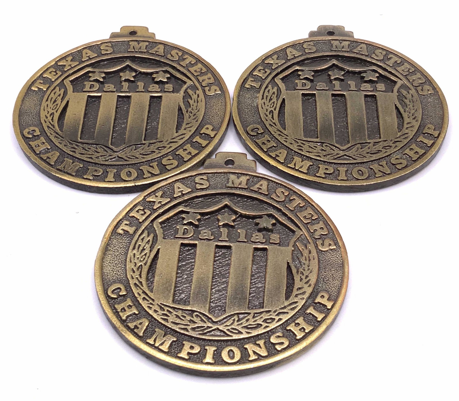 Lot 3 TEXAS MASTERS CHAMPIONSHIP Medals: Three TEXAS MASTERS CHAMPIONSHIP Medals crafted from gold tone metal. Etched and raised metalwork. Bails to the top. Crafted from weighty metal material. Measures approx 2.5L x 2.5W in. Some surface w