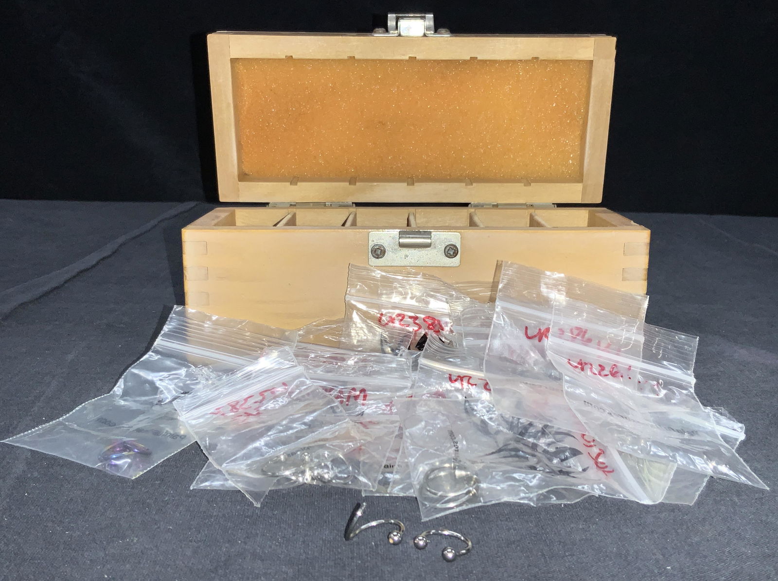 Wooden Box Of Body Jewelry 18 -16G: Wooden box with 6 sections with various hoop piercings and captive beads. Diameters range from 5/16 to 1/2 with gauges from 16 to 18 and possibly 14 gauge. Box is approximately 7 x 3 x 3 inches. Box h