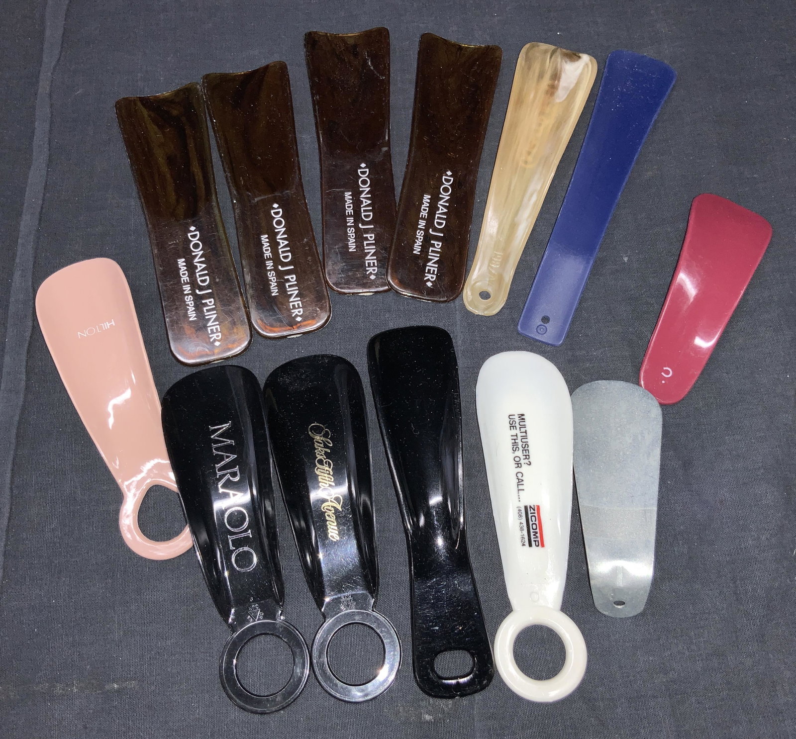 Group Lot 13 Vintage Shoe Horns: Group lot of 13 vintage shoe horns, of varying sizes and materials ranging from white metal, to composite with names such as Marolo, Donald J. planer and Saks Fifth Avenue . Largest is approximately 6