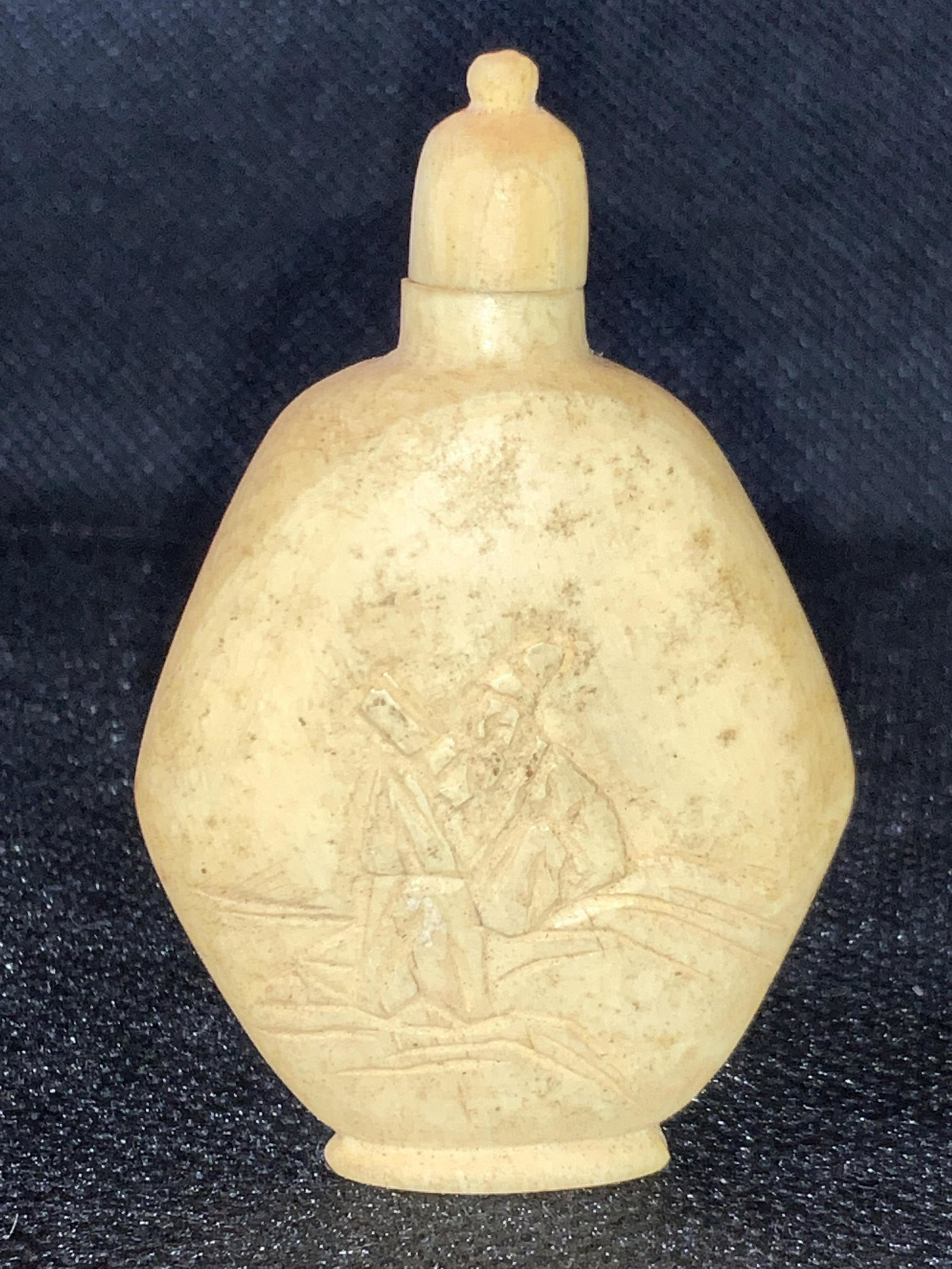 Asian Carved Bone Snuff Bottle: A carved bone / horn snuff bottle. Etched obverse side of a figure in traditional Chinese robes, reverse side is etched with Chinese characters. Cap and bottle appear to be carved from single pieces. 