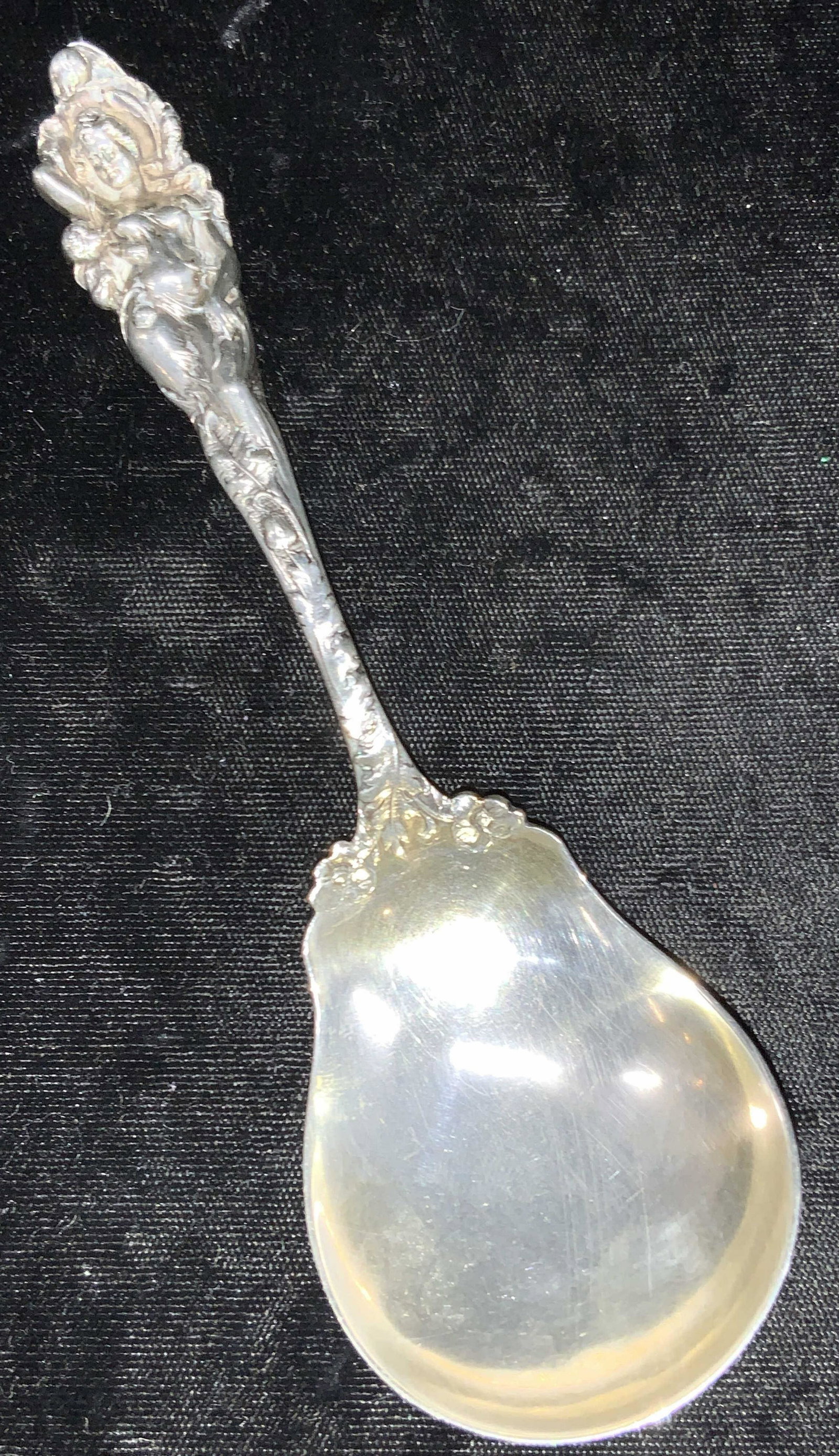 REED & BARTON Embossed Sterling Sugar Spoon: Embossed sterling silver sugar spoon, with the handle embossed to resemble a full figured woman with cherubs and floral motifs. Marked on underside R with lion Passats, Sterling, Pat. A ppld for. Appr